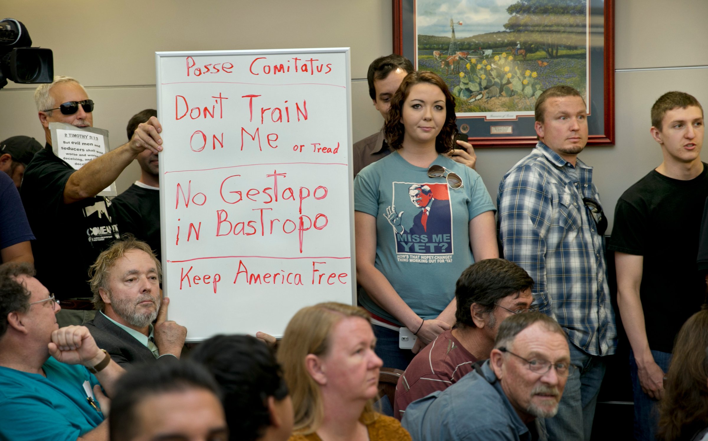 Bob Welch, standing at left, and Jim Dillon, hold a sign at a public hearing about the Jade Helm 15 military training exercise in Bastrop, Texas, April 27, 2015