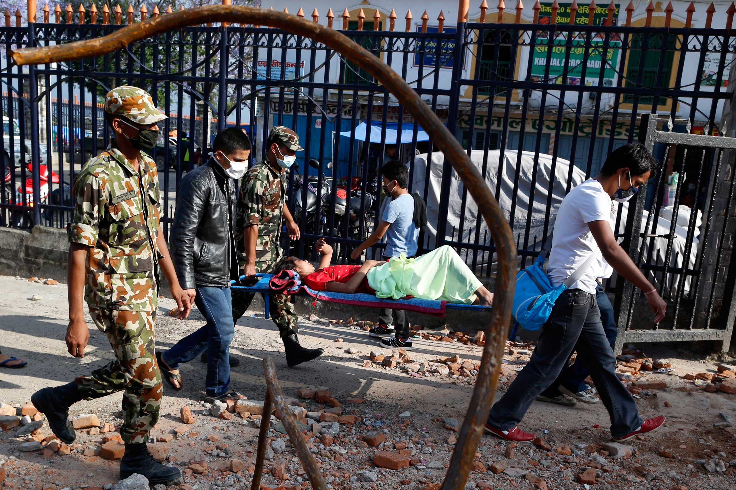 A patient is carried by Nepalese military personnel and volunteers back to the hospital building after she had been evacuated when an earthquake hit, in Kathmandu on May 12, 2015.
