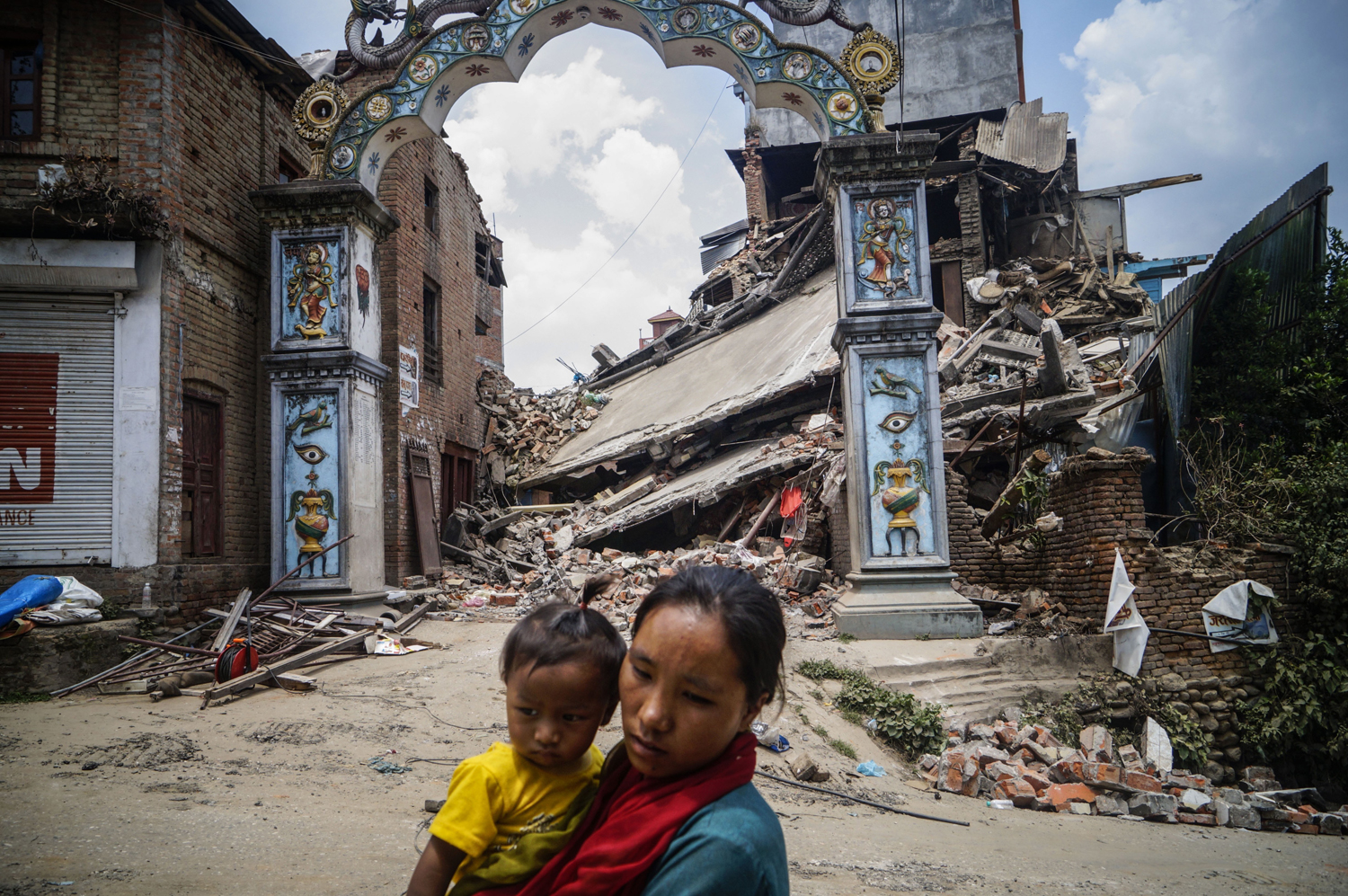 A Nepalese woman carrying her child walks past a destroyed building in Sankhu village in Kathmandu, Nepal on May 16, 2015. (Anadolu Agency —Getty Images)