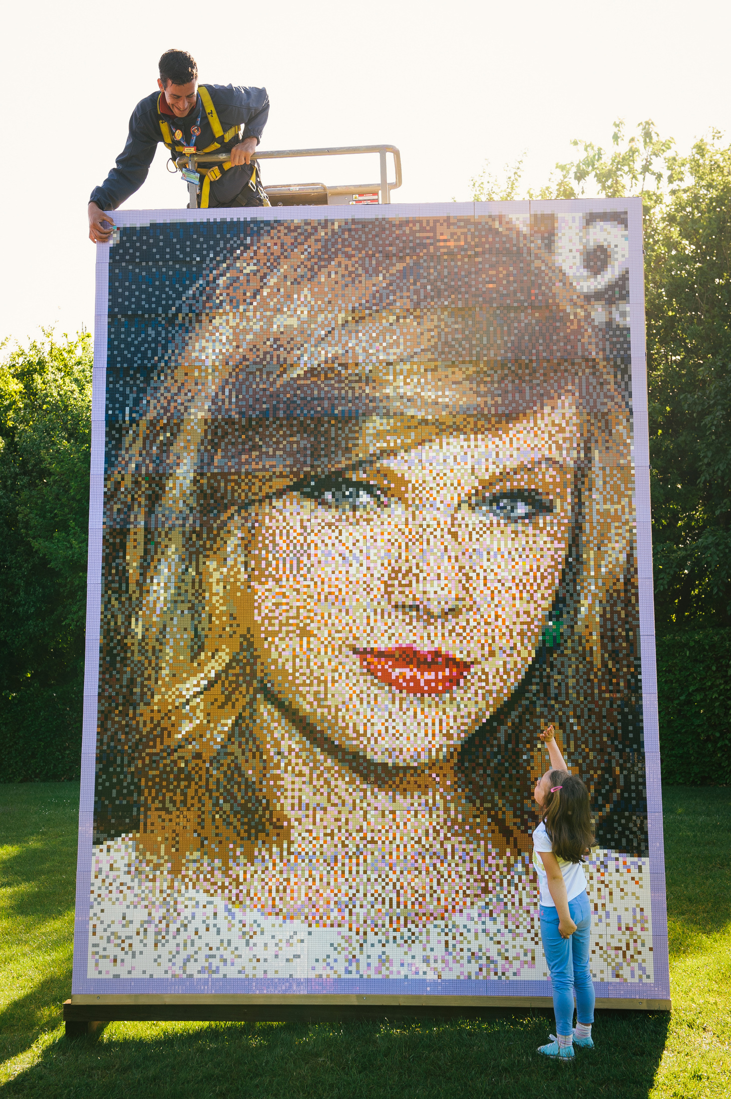 In this handout photo provided by Legoland, Kitty Baker, age 5, looks up at Legoland employee Pete Goodchild as he puts the finishing touches on the mosaic of 'Celebrity Best Friend' Taylor Swift at The Legoland Windsor Resort on May 25, 2015 in Windsor, England.