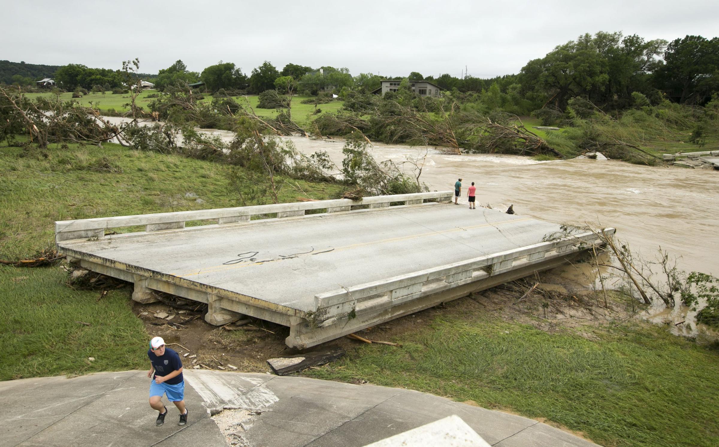 Dustin McClintock, Brandon Bankston, and Hesston Krause look at the destroyed remains of the Fischer Store Road bridge over the Blanco River near Wimberley, Texas on May 24, 2015.