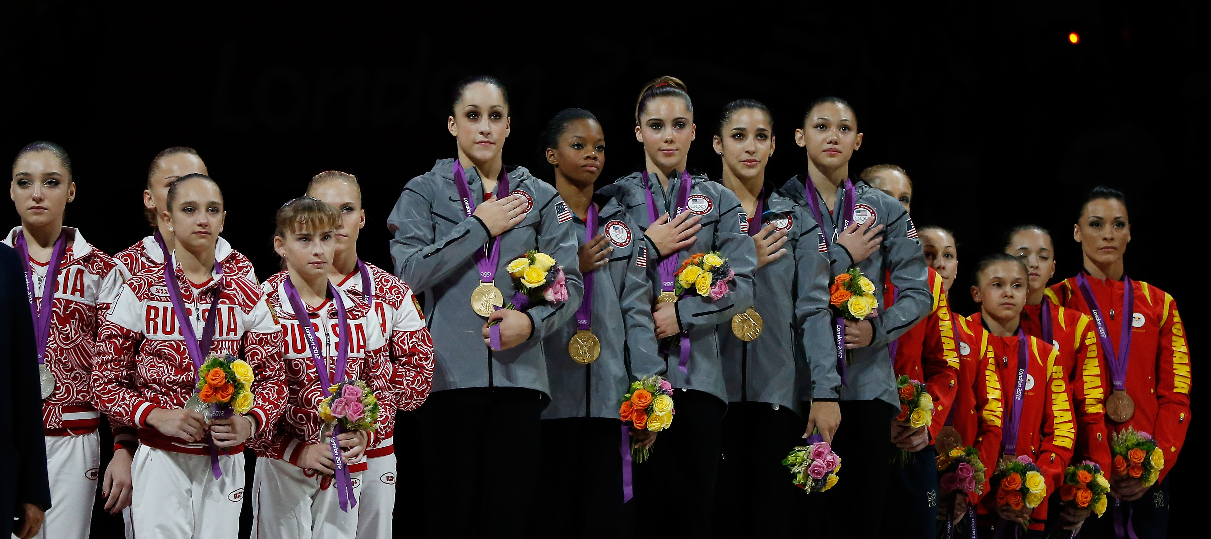 Silver medalists Russia, gold medalists United States with Aly Raisman second from right, and bronze medalists Romania pose of the podium after the Artistic Gymnastics Women's Team final on Day 4 of the London 2012 Olympic Games at North Greenwich Arena on July 31, 2012 in London. (Jamie Squire—Getty Images)