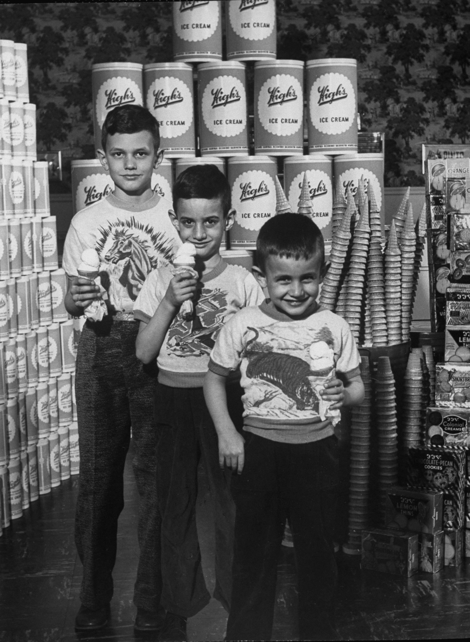 Charles, Stephen and Kenneth Winston standing with cartons of ice cream, cones and cookies representing a year's consumption, 1953.