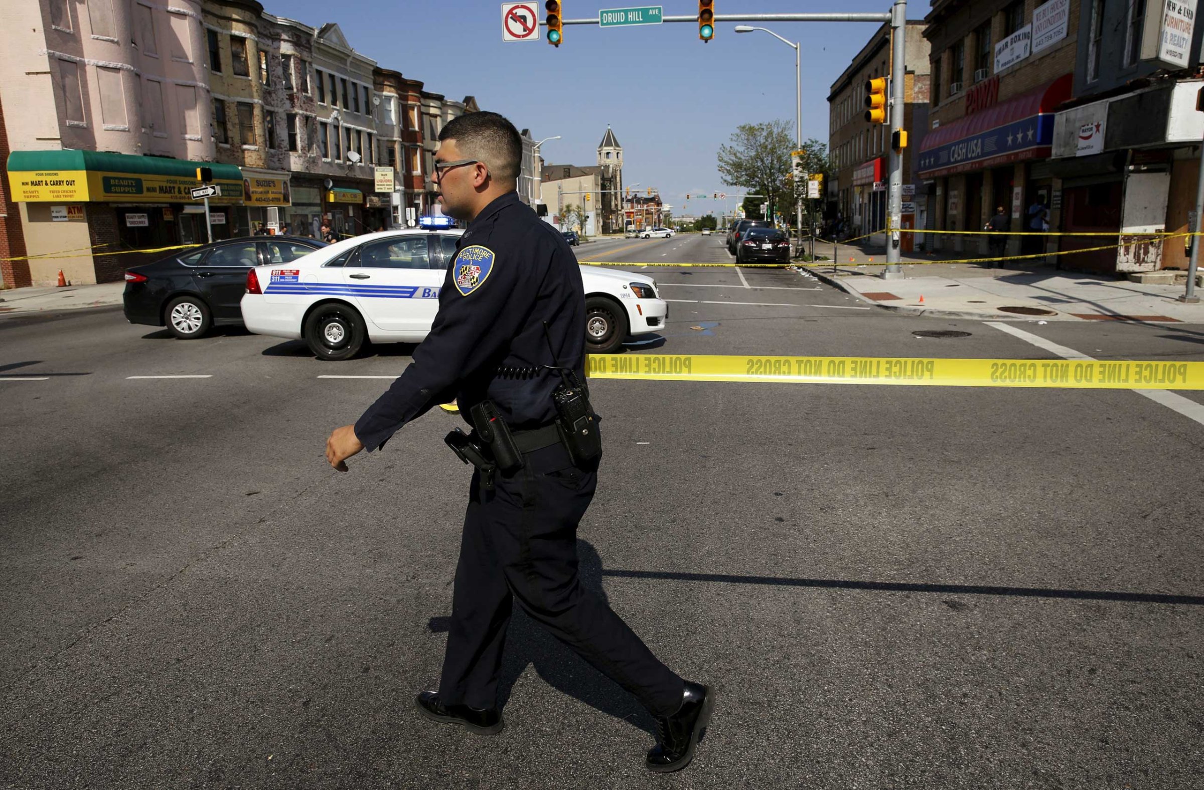 Baltimore police officer attempts to secure a crime scene with tape at the scene of a shooting in West Baltimore