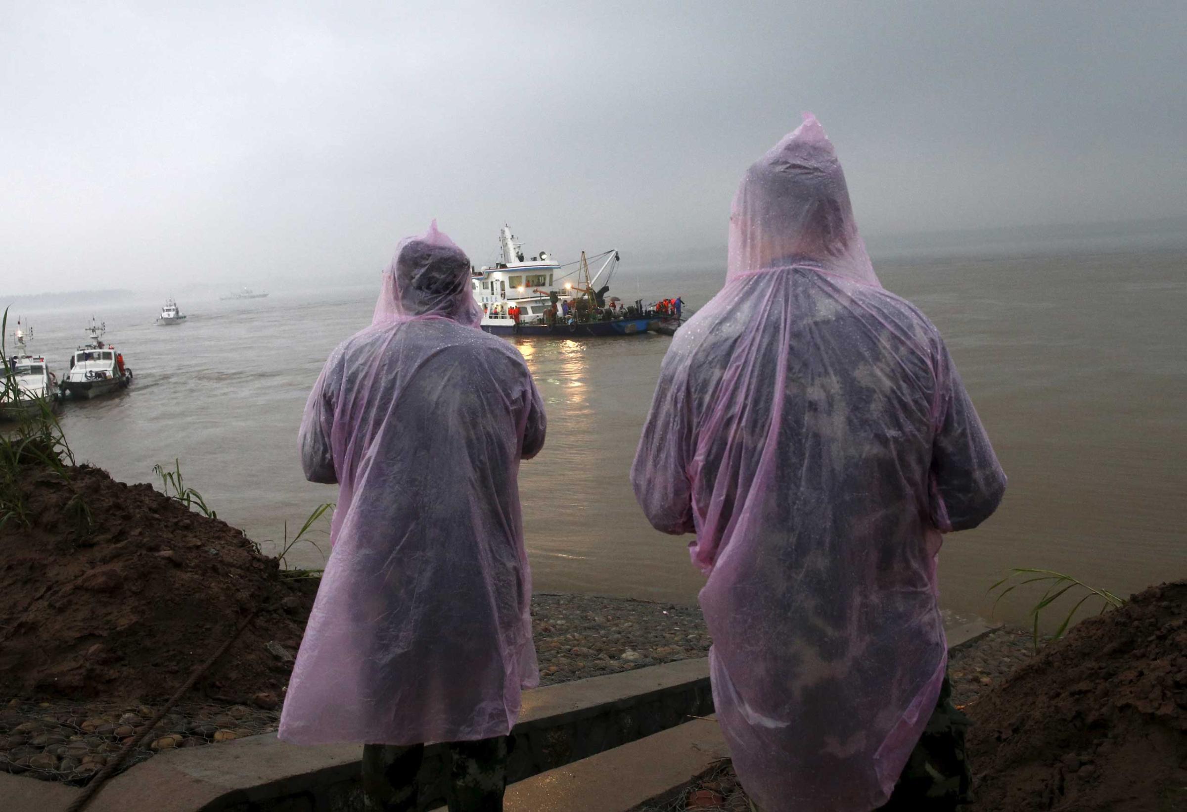 Paramilitary soldiers in raincoats watch a sunken ship and rescue ship in the Jianli section of Yangtze River, Hubei province, China on June 2, 2015.