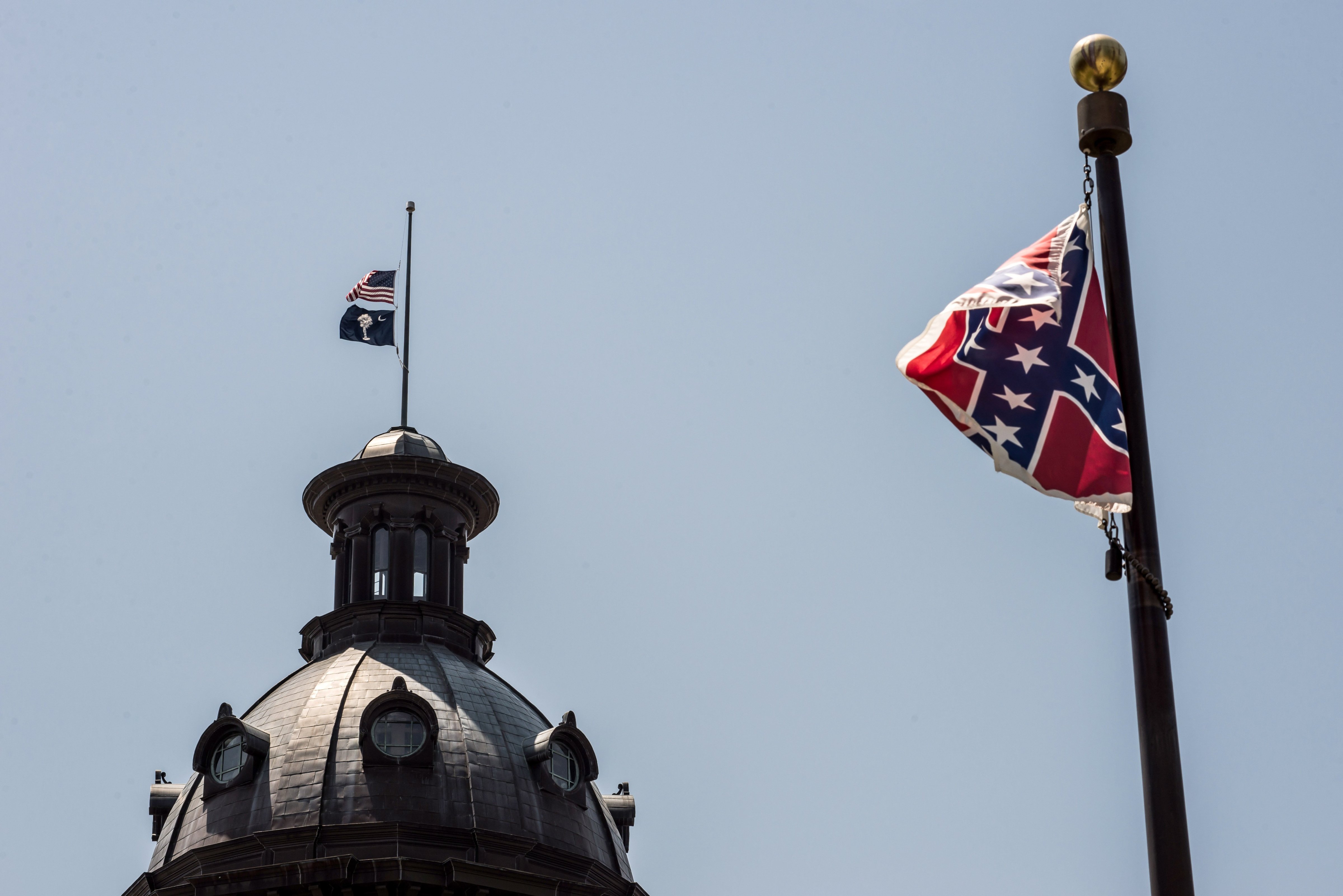 The South Carolina and American flags fly at half mast as the Confederate flag unfurls below at the Confederate Monument June 18, 2015 in Columbia, South Carolina.