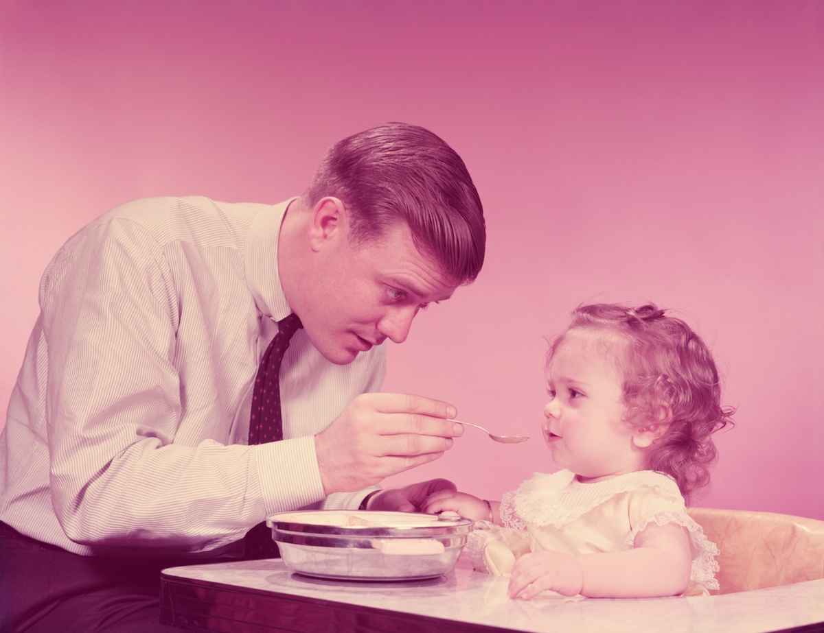 Father feeding daughter sitting in high chair