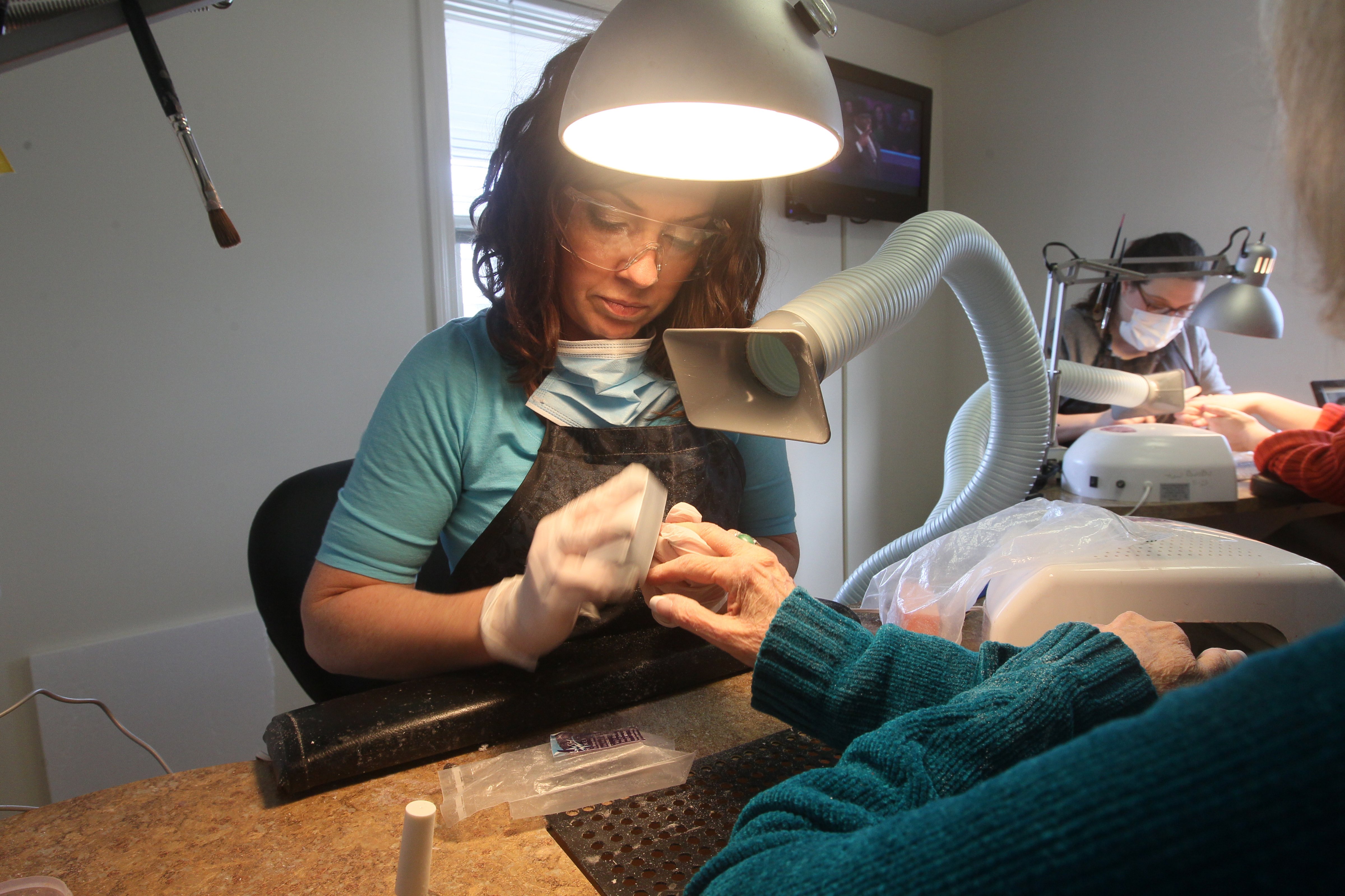 Nail technician Kellie Deagazio uses a nail ventilation system as she applies acrylics to customer Adrienne Wilson of Brookline at Forever French Salon in Norwood. (Joanne Rathe—Boston Globe/Getty Images)