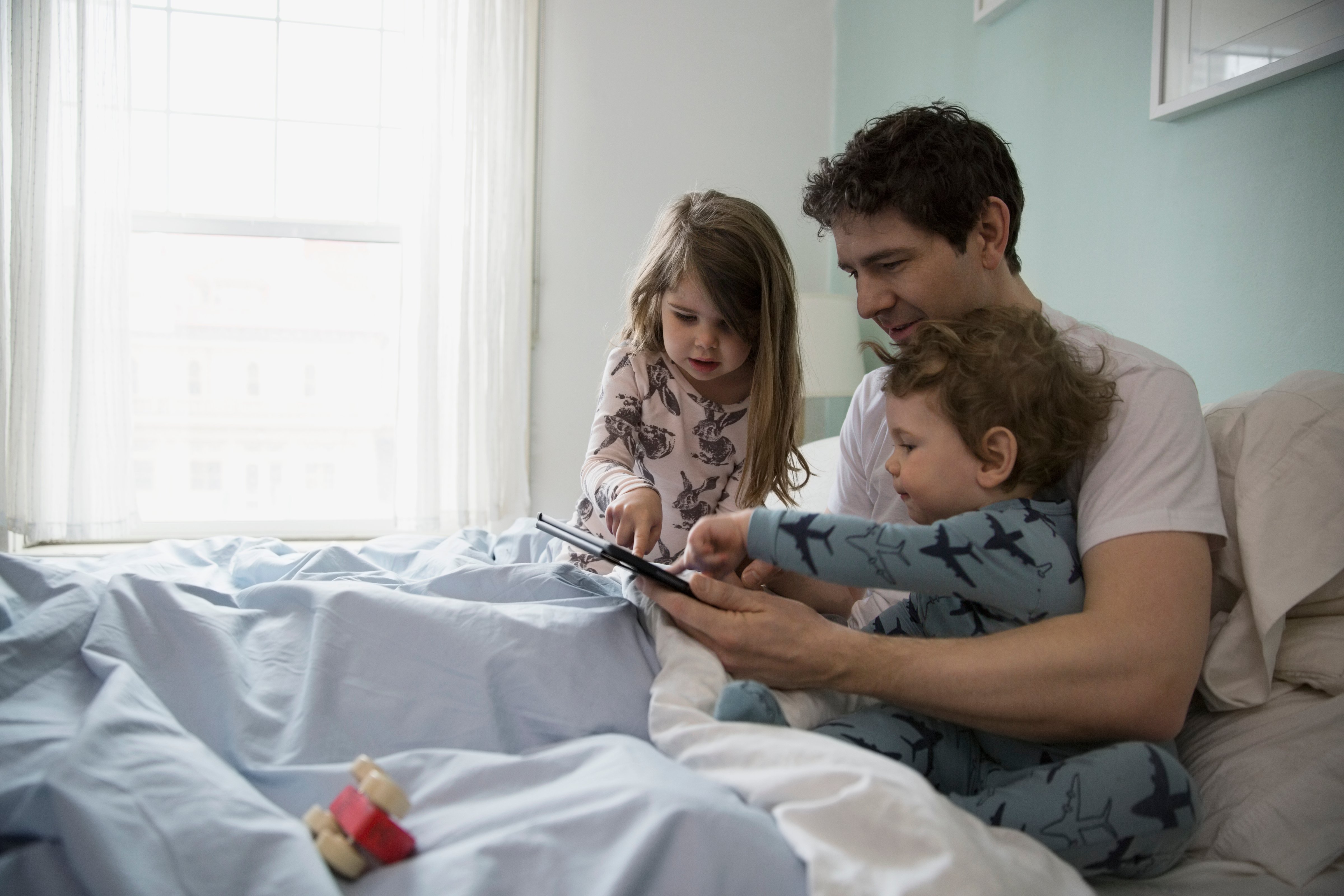Father and children using digital tablet in bed (Hero Images&mdash;Getty Images/Hero Images)