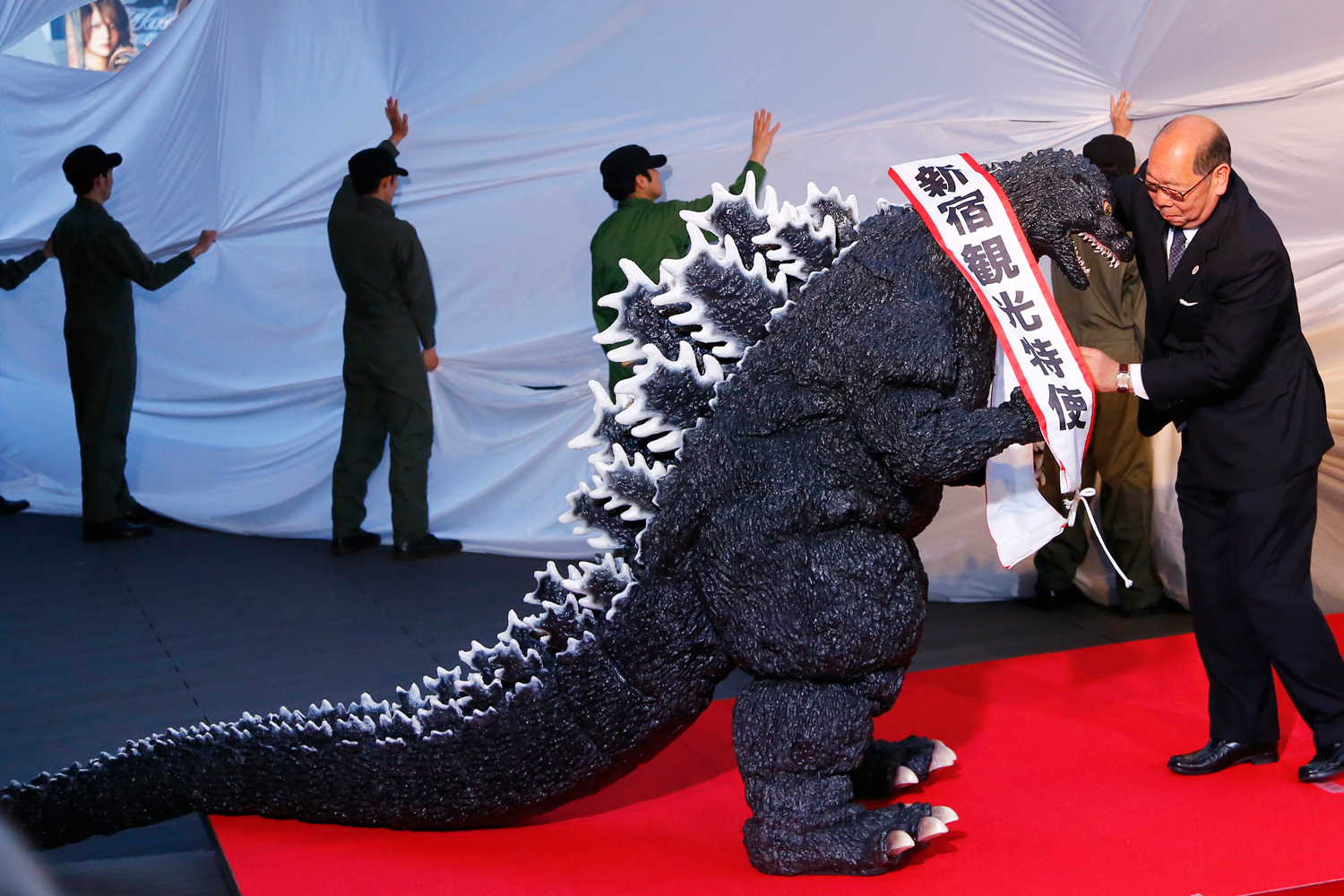 Godzilla gets a sash of "Shinjuku-ward tourism ambassador" from the Kabuki-cho Shopping Area Promotion Association Chief Director Mototsugu Katagiri of Tokyo's Shinjuku-ward during its awards ceremony in Tokyo, April 9, 2015. (Shizuo Kambayashi—AP)