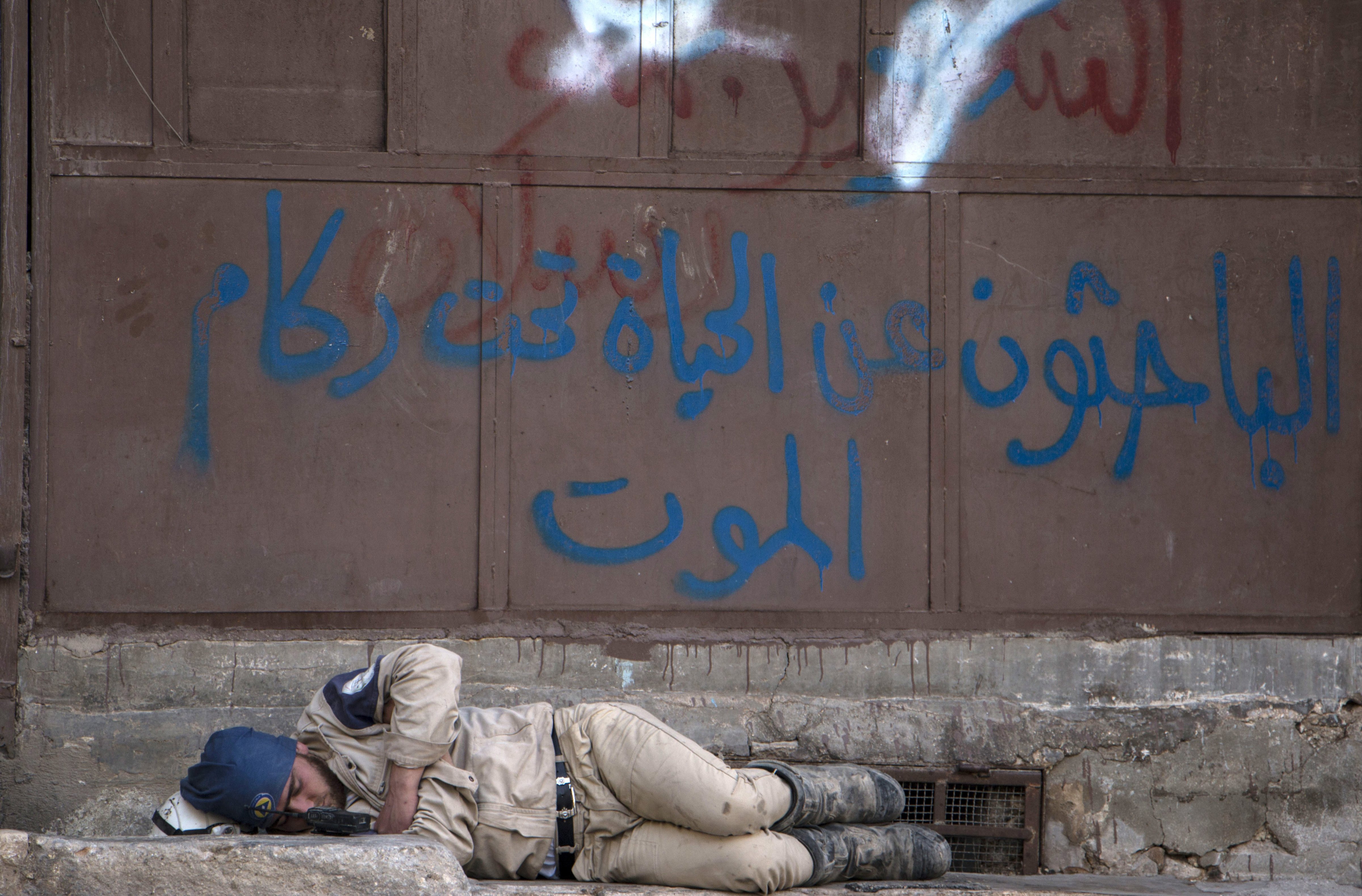 A member of the civil defense sleeps on the street in the rebel-held side of Syria's northern city of Aleppo on June 8, 2015, the Arabic graffiti in blue reads: "Those looking for life under the rubble of death". (Karam Al-Masri—AFP/Getty Images)