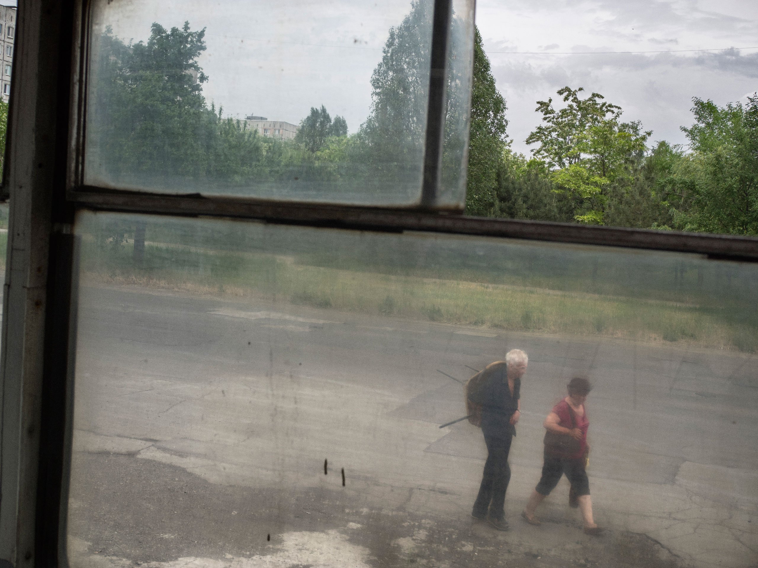 Two elderly people walk, as seen through a window on the tramway. Mariupol, Ukraine. May 28, 2015.