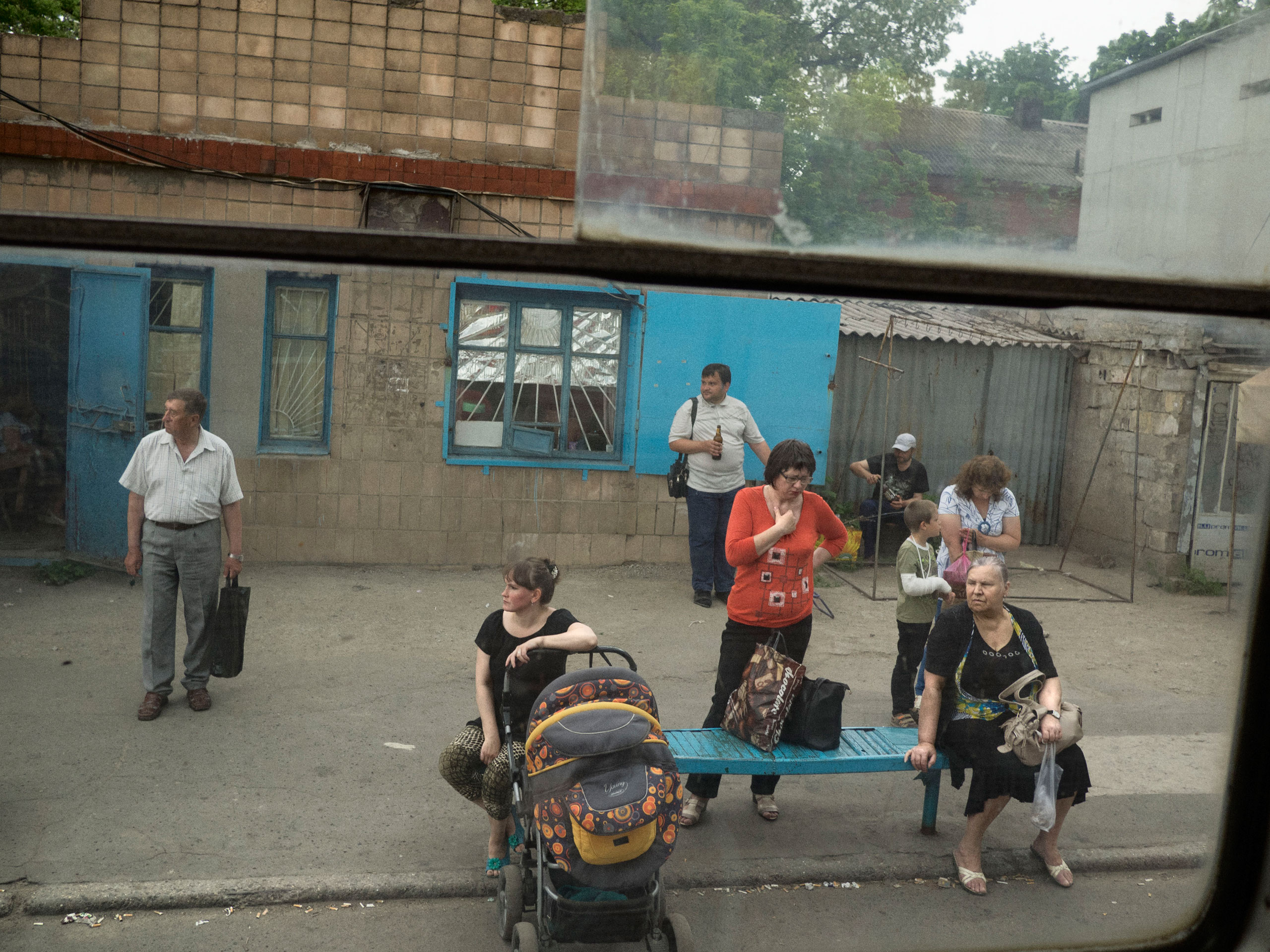 A view of people waiting at the main station of the tramway in the downtown area, as seen through a window on the tramway. Mariupol, Ukraine. May 28, 2015.