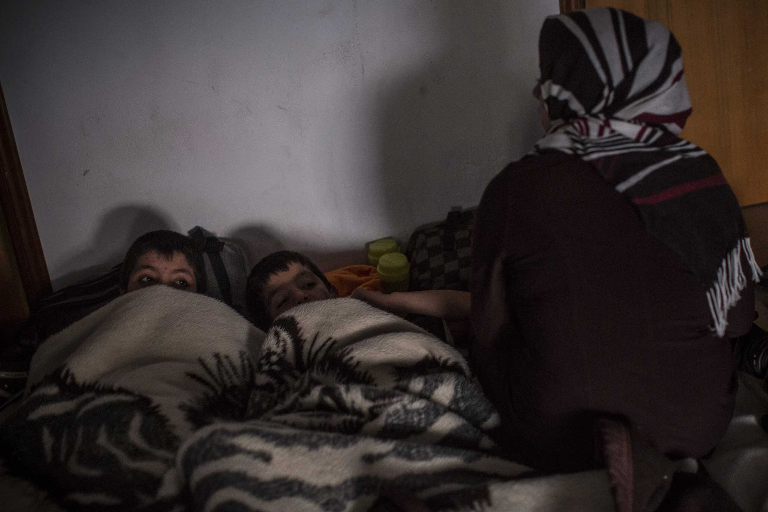 A mother sits with her two young sons as they get ready to sleep in the corridor of an abandoned hotel that many migrants are using as a temporary shelter on the Greek island of Kos on May 30, 2015.