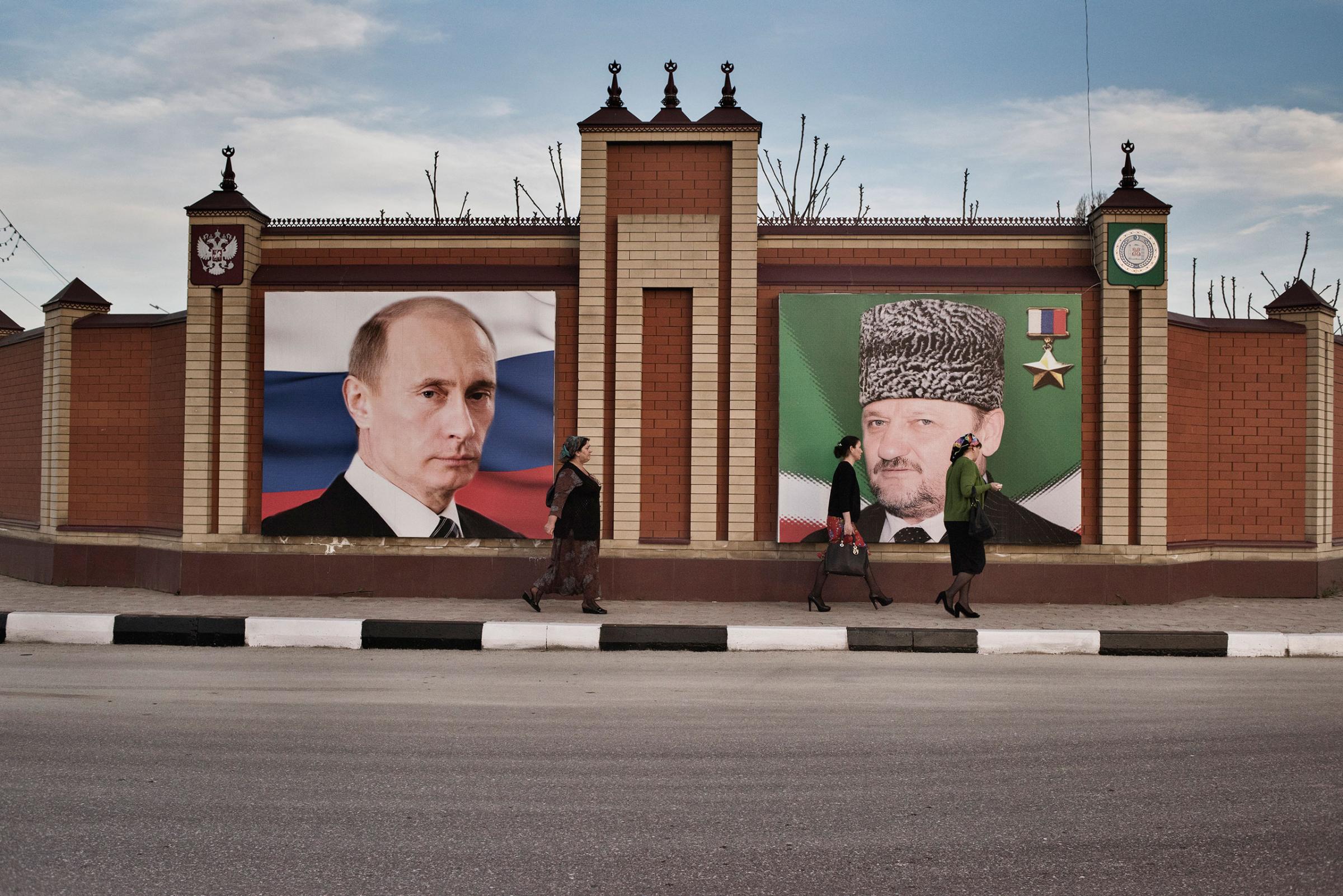 Women pass by a portrait of Russian President Vladimir Putin and the late President of Chechnya Akhmat Kadyrov in Grozny, Chechnya, April 18, 2015.