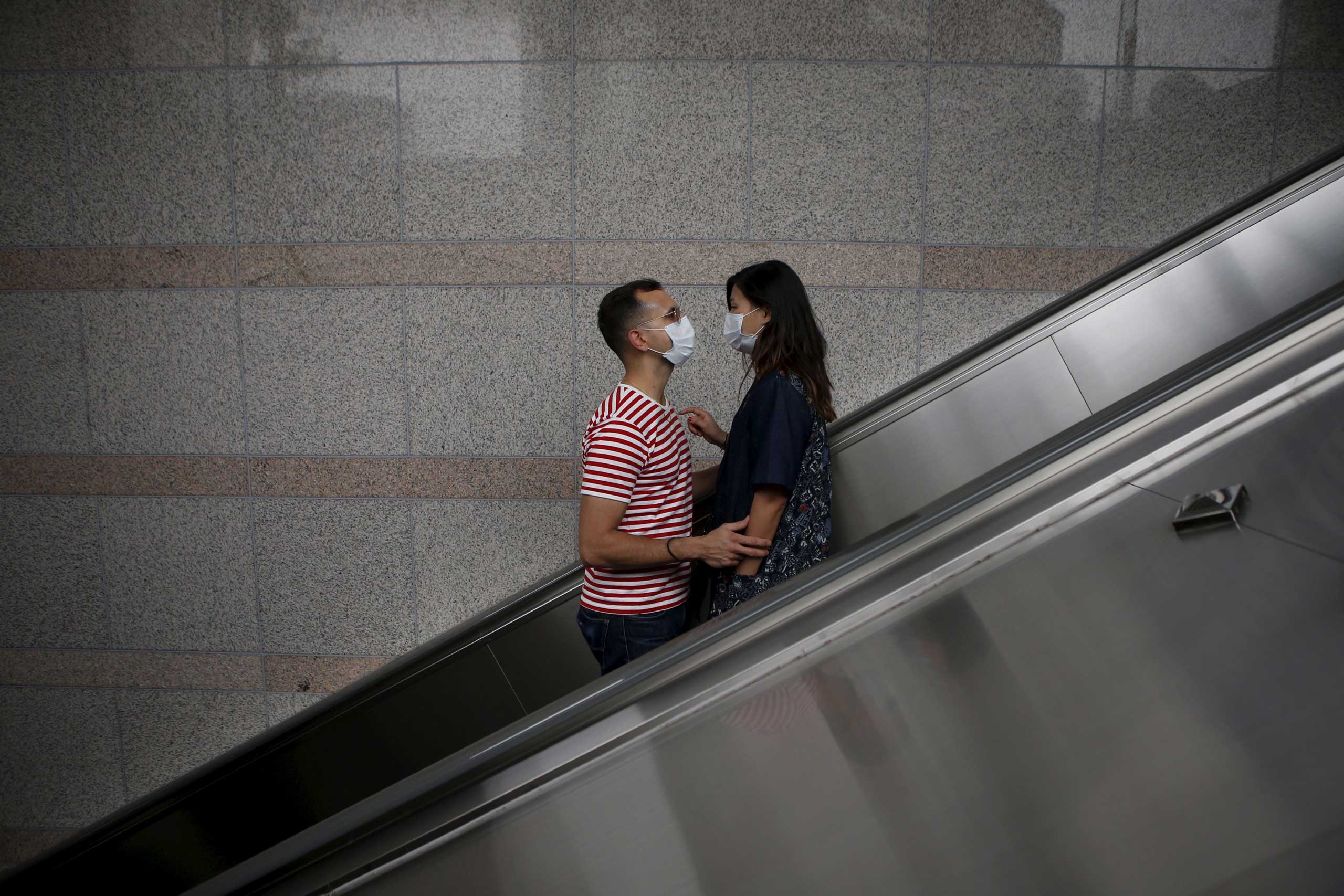 A couple wearing masks looks at each other as they ride on an escalator in Seoul on June 11, 2015.