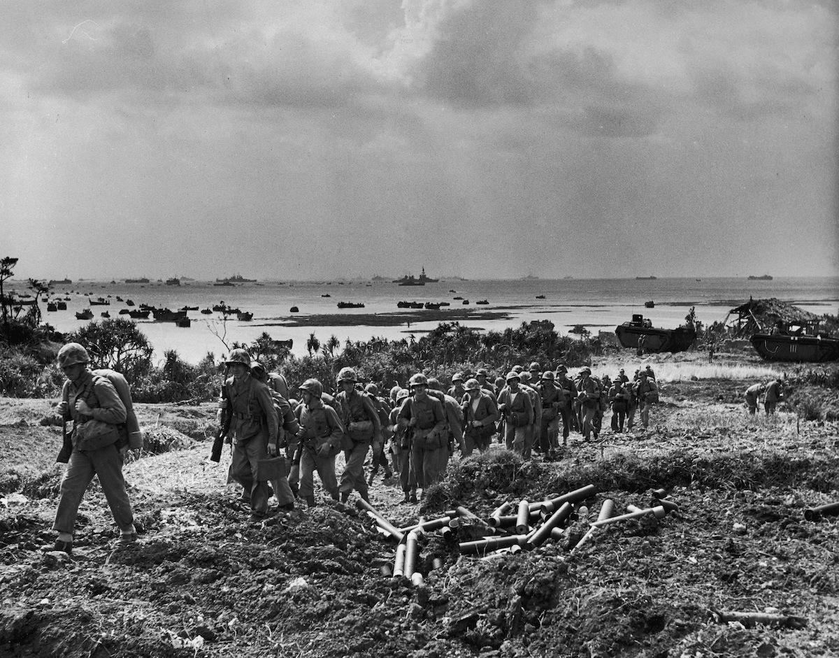 Soldiers of US 10th Army march inland after securing beachheads following the last amphibious assault landings of WWII as vessels from the Allied fleet patrol the waters off of Okinawa, Japan, April 1945. (J. R. Eyerman—The LIFE Picture Collection/Getty Images)