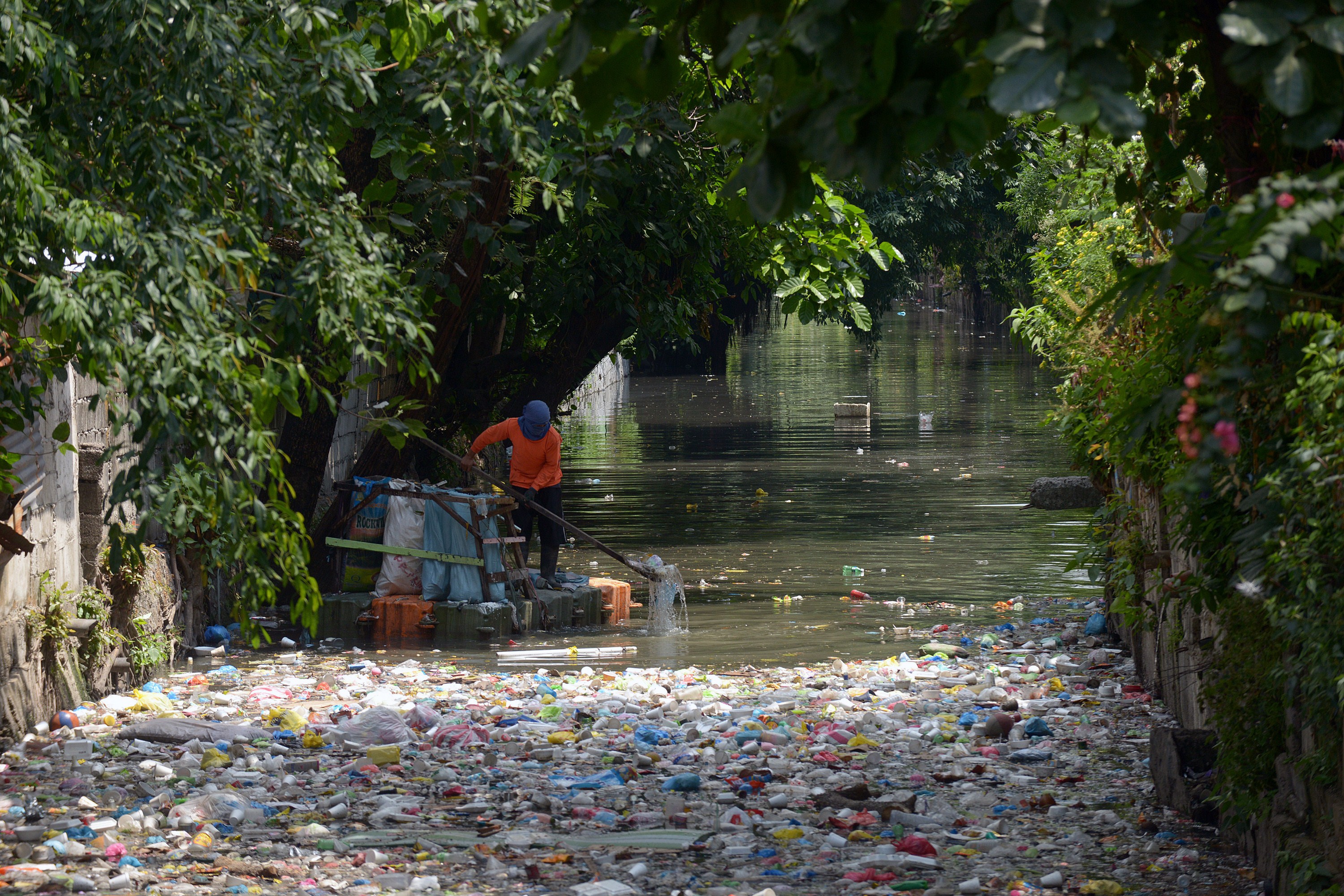 A clean-up volunteer scoops plastic waste at an open sewer in Manila on May 4, 2015. Non-governmental environmental groups are calling for national legislation to prevent plastic waste that clog waterways.