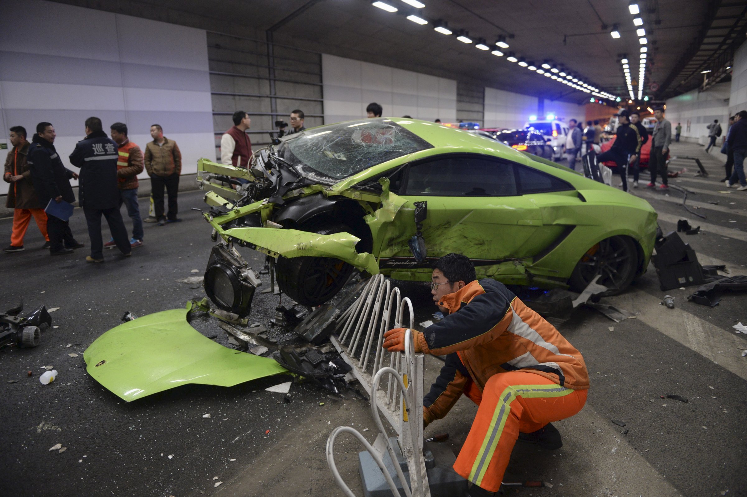 A rescuer tries to remove a part of a broken fence below a damaged Lamborghini after it collided with a Ferrari inside a tunnel in Beijing