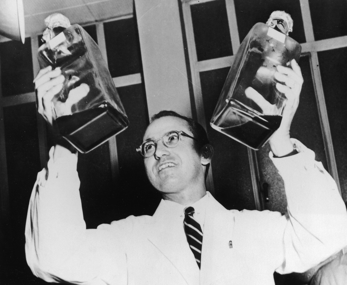 Jonas Salk (1914 - 1995) holding up two decanters containing the anti-polio vaccine that he developed. (Archive Photos/Getty Images)
