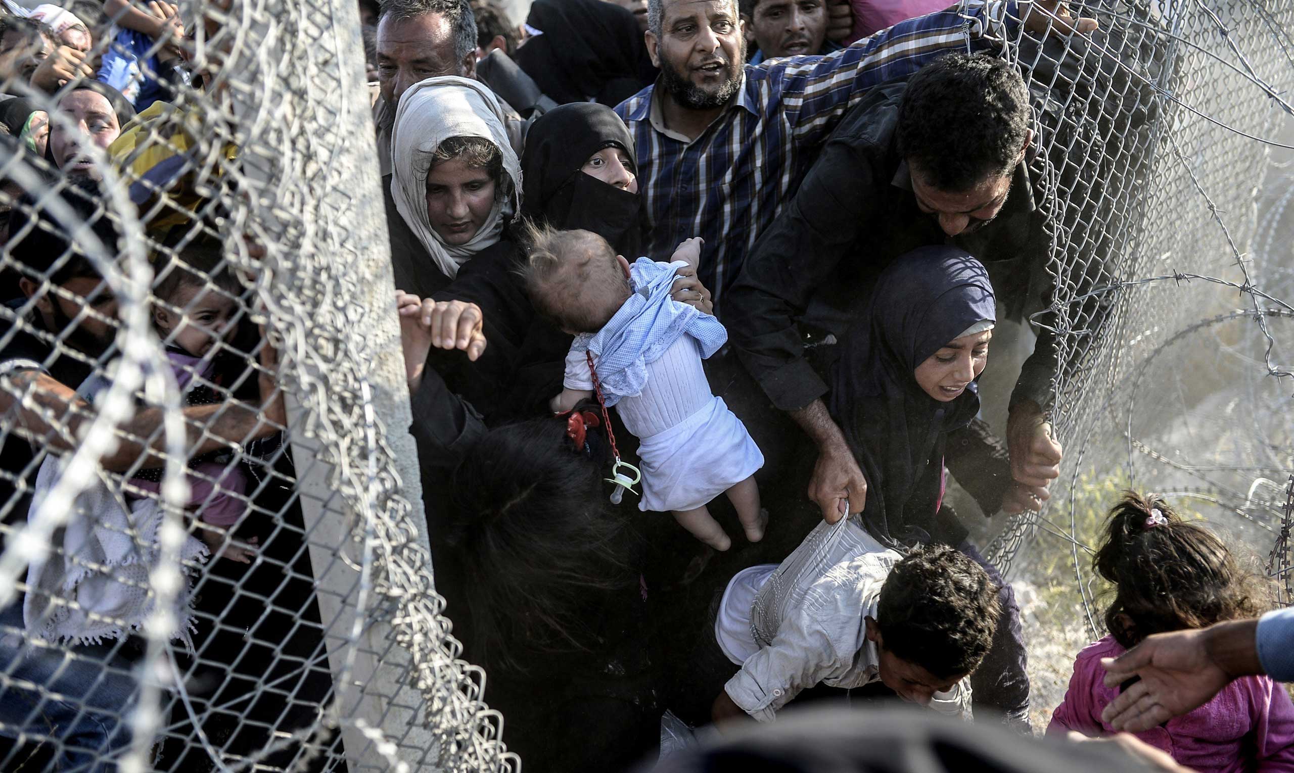 Syrians flee the war rush through broken down border fences to enter Turkish territory illegally, near the crossing at Akçakale in Sanliurfa province, on June 14, 2015.