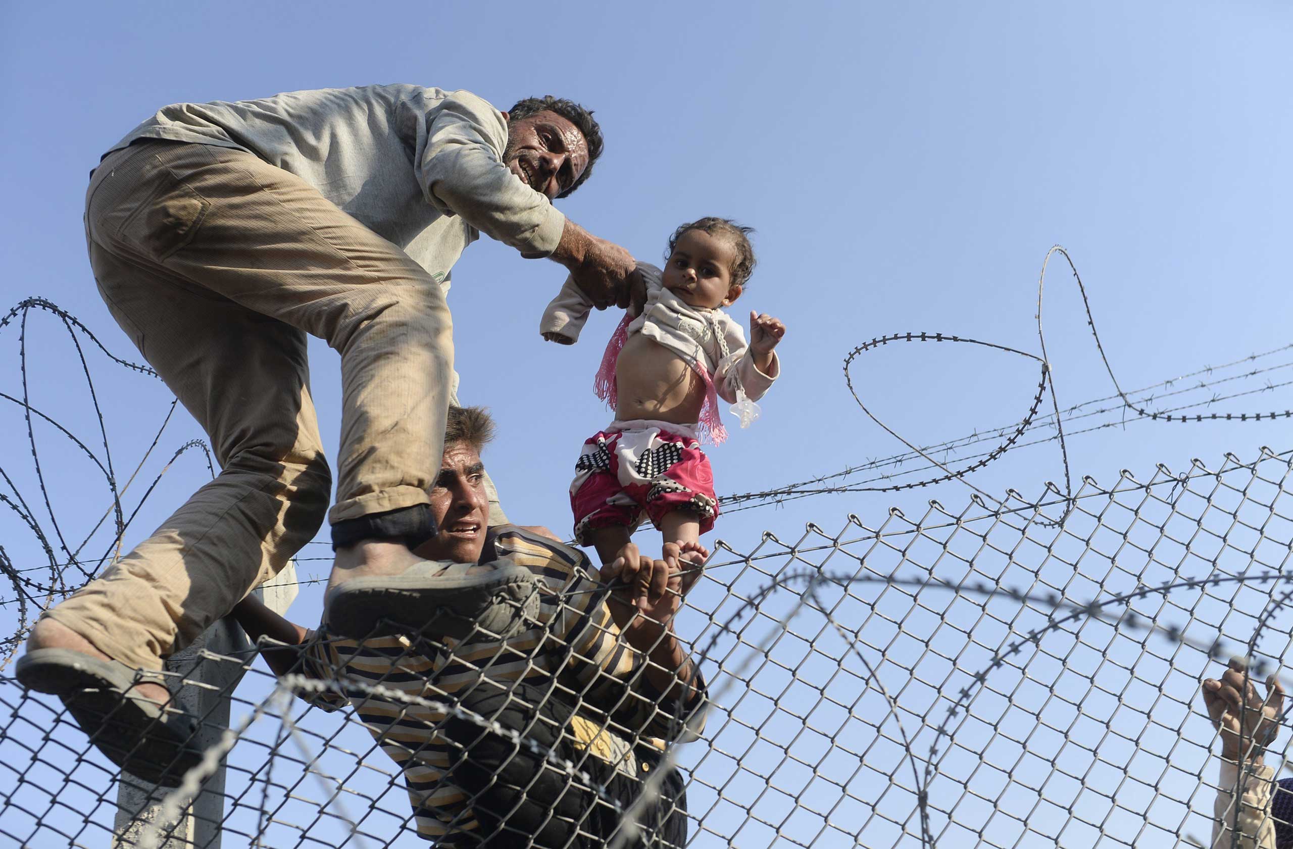 A Syrian child fleeing the war is lifted over border fence to illegally enter Turkish territory, near the Turkish border crossing at Akçakale, in Sanliurfa province, on June 14, 2015.