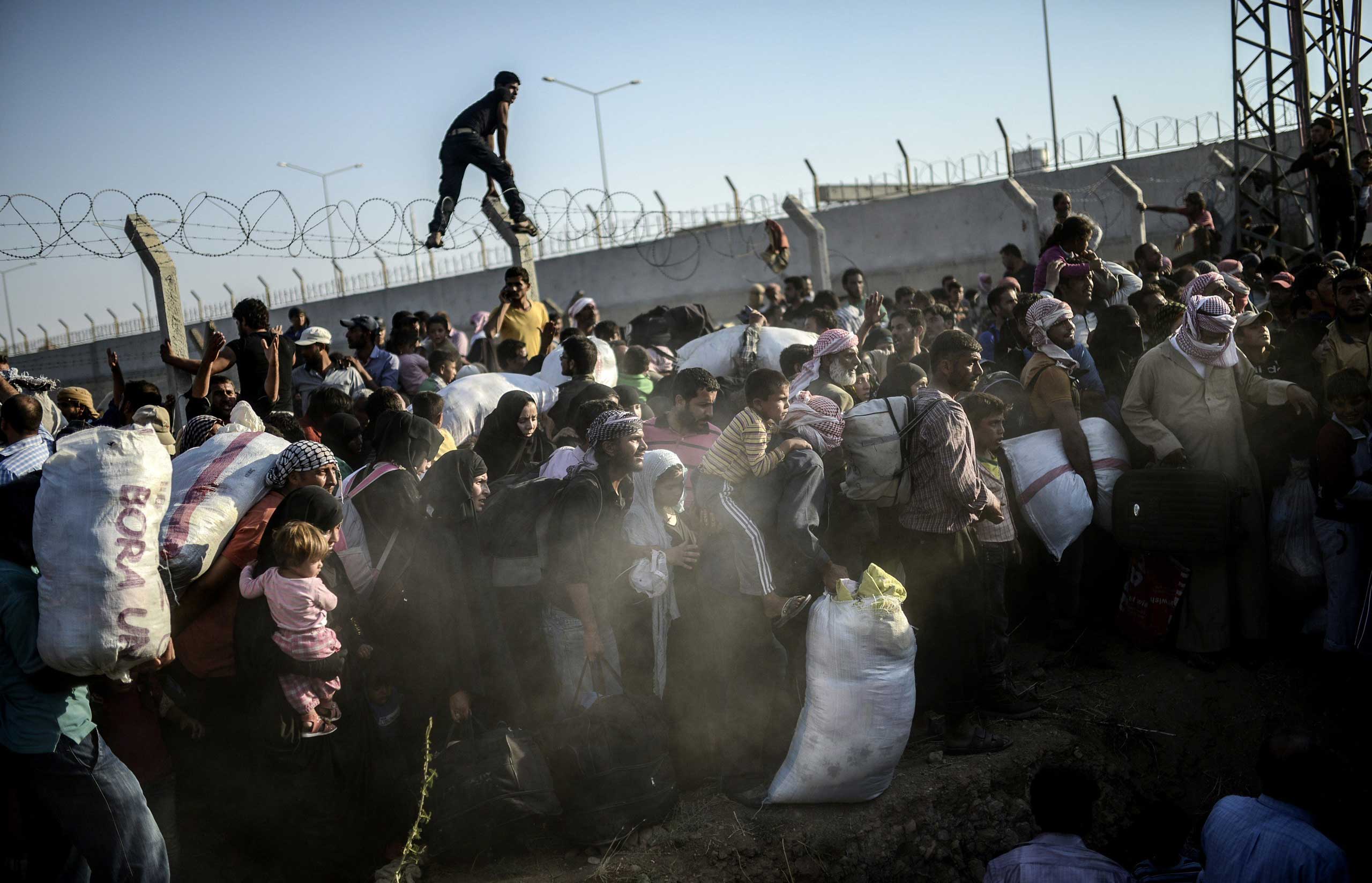 Syrians fleeing the war pass through broken border fences to illegally enter Turkish territory, near the Turkish border crossing at Akçakale, in Sanliurfa province, on June 14, 2015.