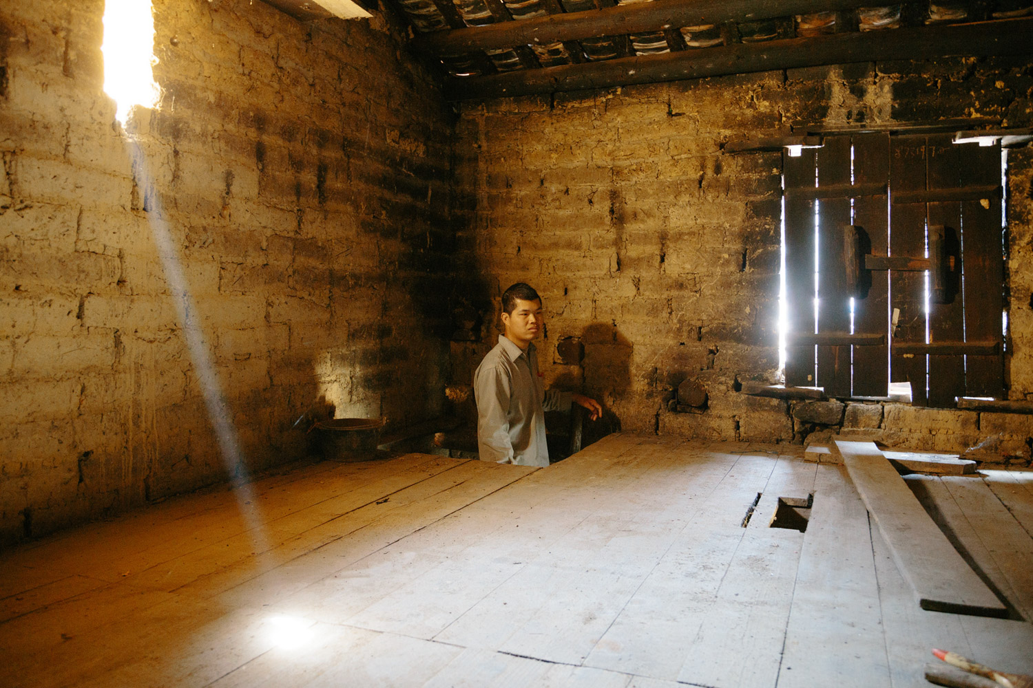 Jiagui Su stands on a ladder to the loft of his adobe where his