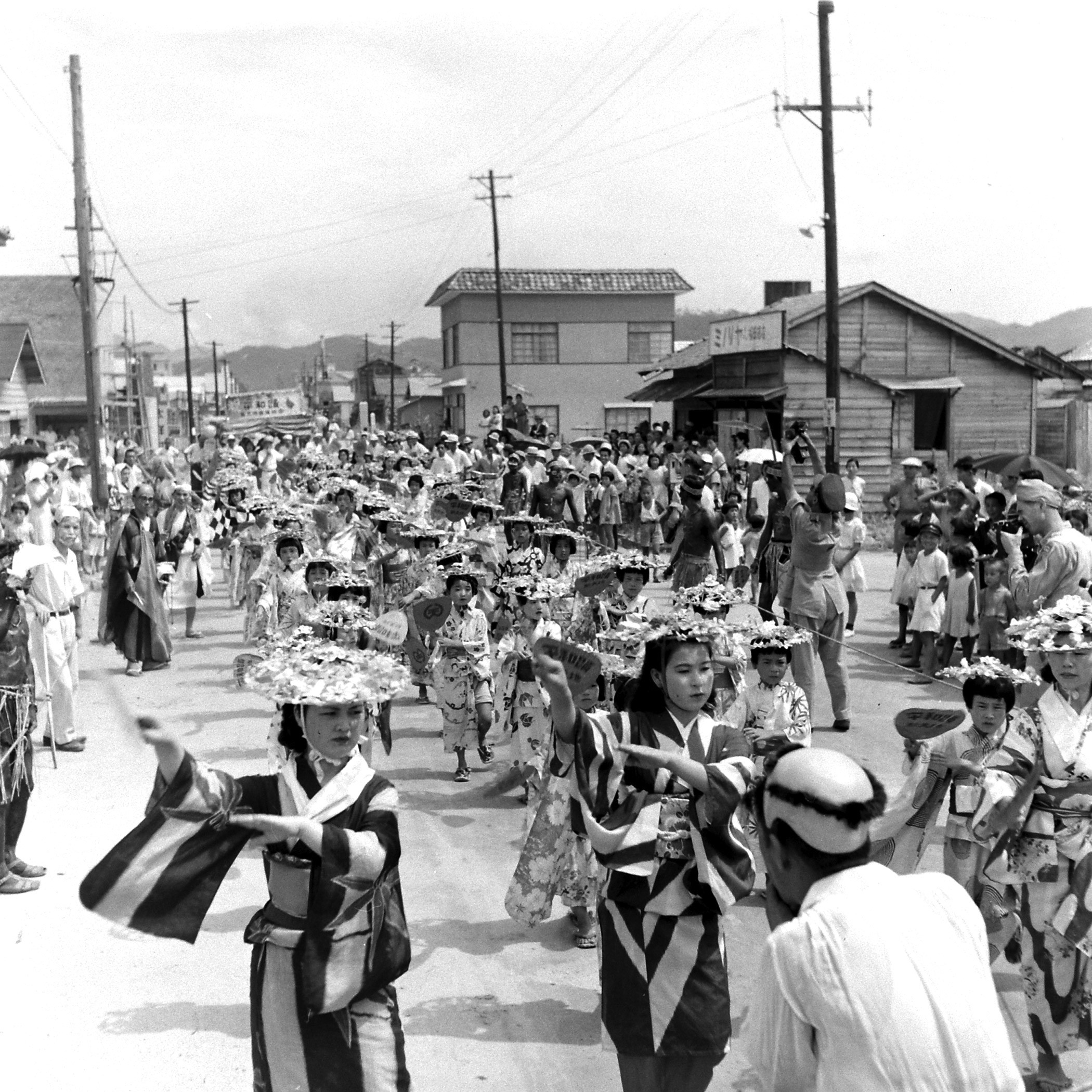 Peace procession headed by gaily clad dancing girls streams through the city. Soon after solemn services Hiroshima was filled with a carnival atmosphere.