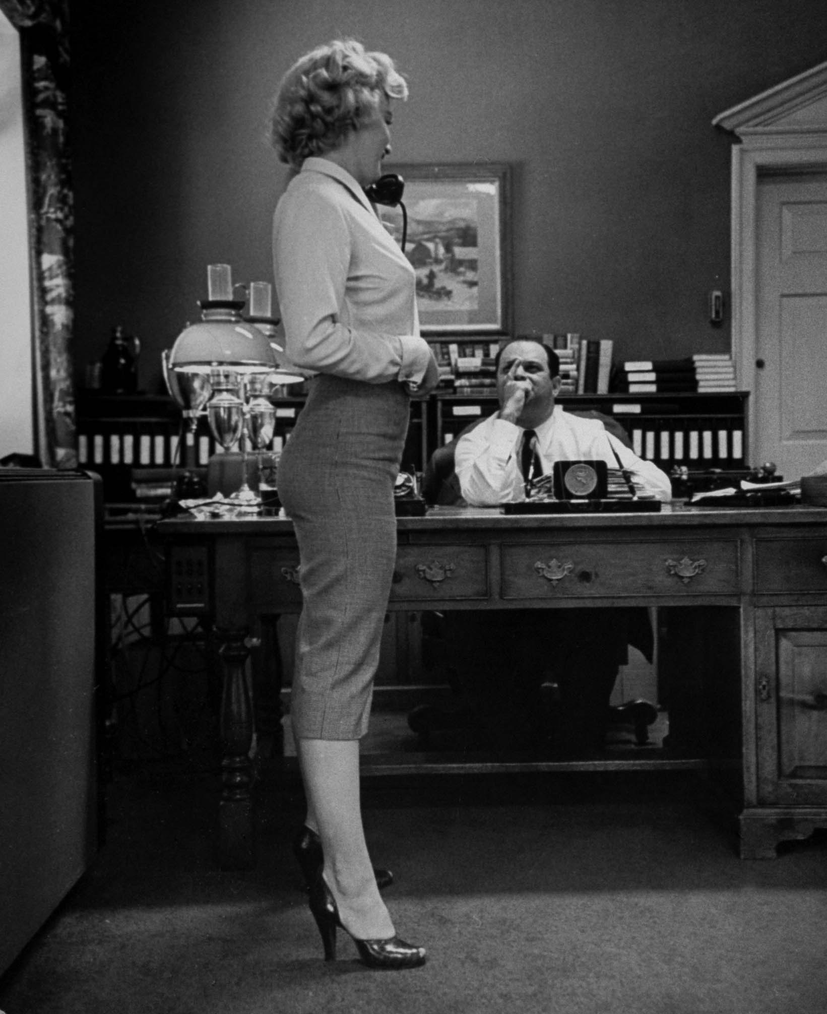 Marilyn Monroe talking on the phone while displaying her talents for movie producer Jerry Wald who is interviewing her for a role in Clifford Odets movie "Clash by Night" which he is producing, in his office. 1951.