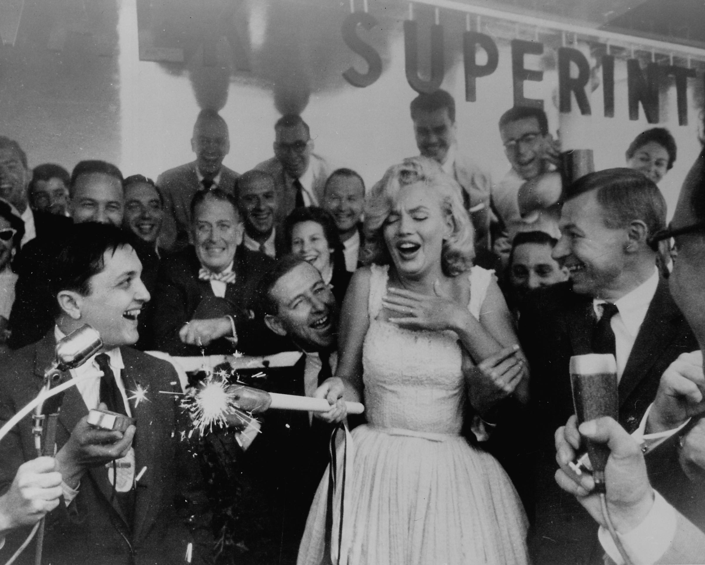 Marilyn Monroe looking startled while holding flaming sparkler in the Rockefeller Center Sidewalk Superintendents Club during ceremony for soon to be built Time &amp; Life Building as others look on., 1957.