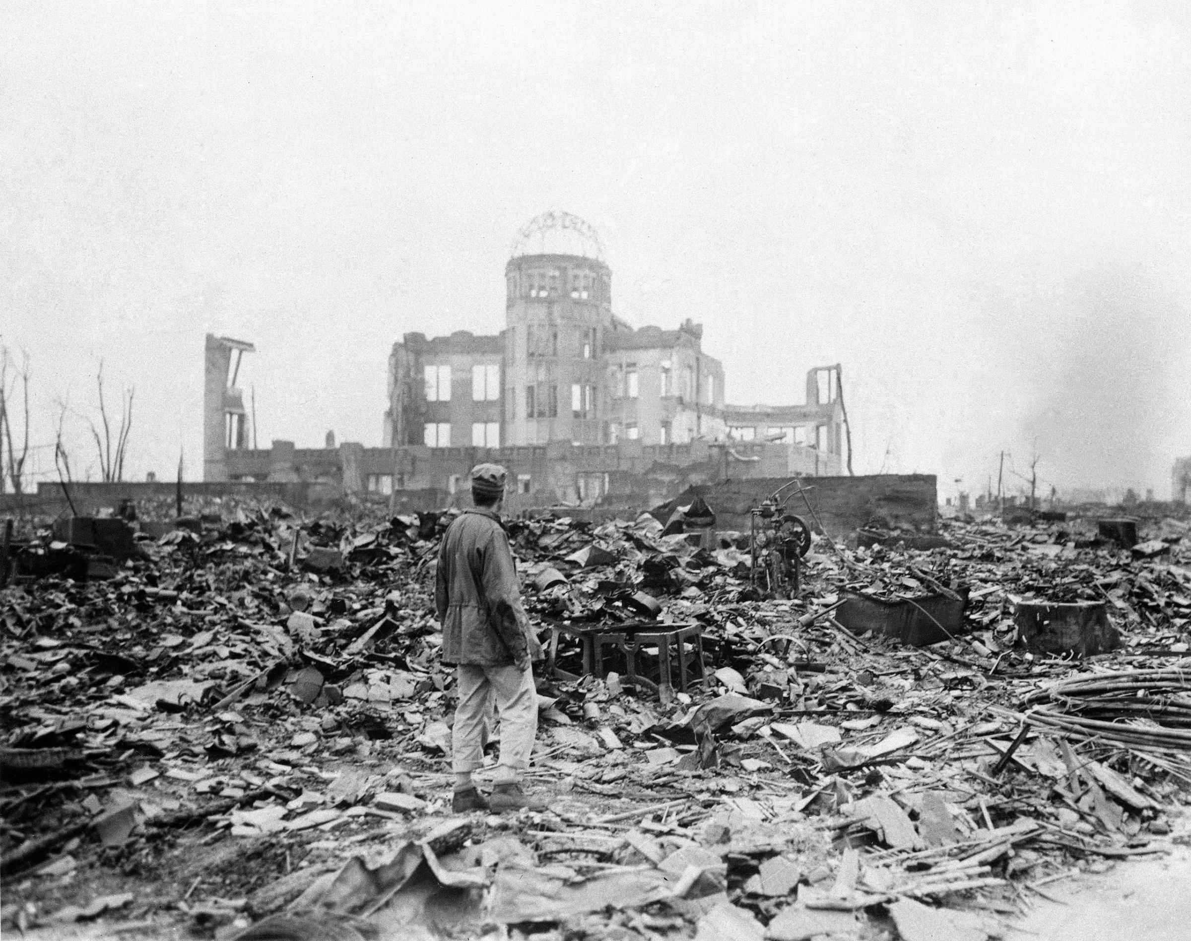 September 8, 1945, an allied correspondent stands in the rubble in front of the shell of a building that once was a movie theater in Hiroshima, Japan, a month after the first atomic bomb ever used in warfare was dropped by the U.S. on Aug. 6, 1945.The damaged building standing in the background is the Hiroshima Prefectural Industrial Promotion Hall, currently preserved as the Atomic Bomb Dome.