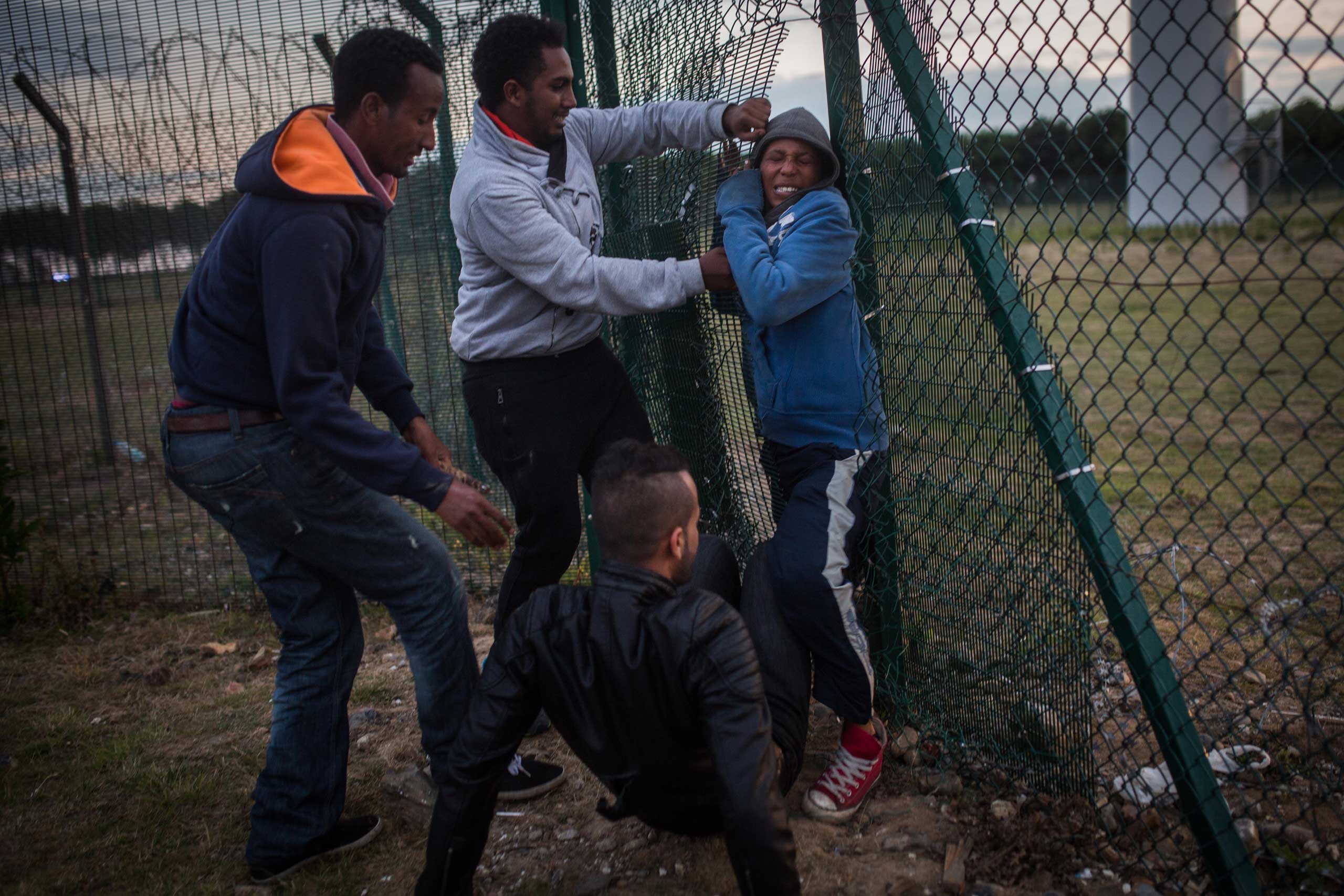 People help a young man squeeze through a gap in a fence near the Eurotunnel terminal in Coquelles in Calais, France, on July 30, 2015. (Rob Stothard—Getty Images)