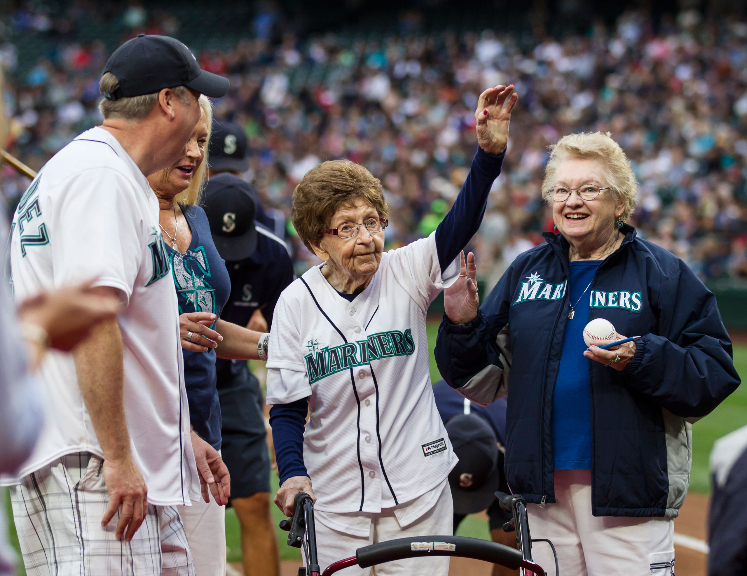 108-year-old Evelyn Jones, center, of Woodinville, Wash., waves to the crowd after throwing out the ceremonial first pitch on her birthday before a baseball game between the Seattle Mariners and the Los Angeles Angels, Saturday, July 11, 2015, in Seattle. (AP Photo/Stephen Brashear)