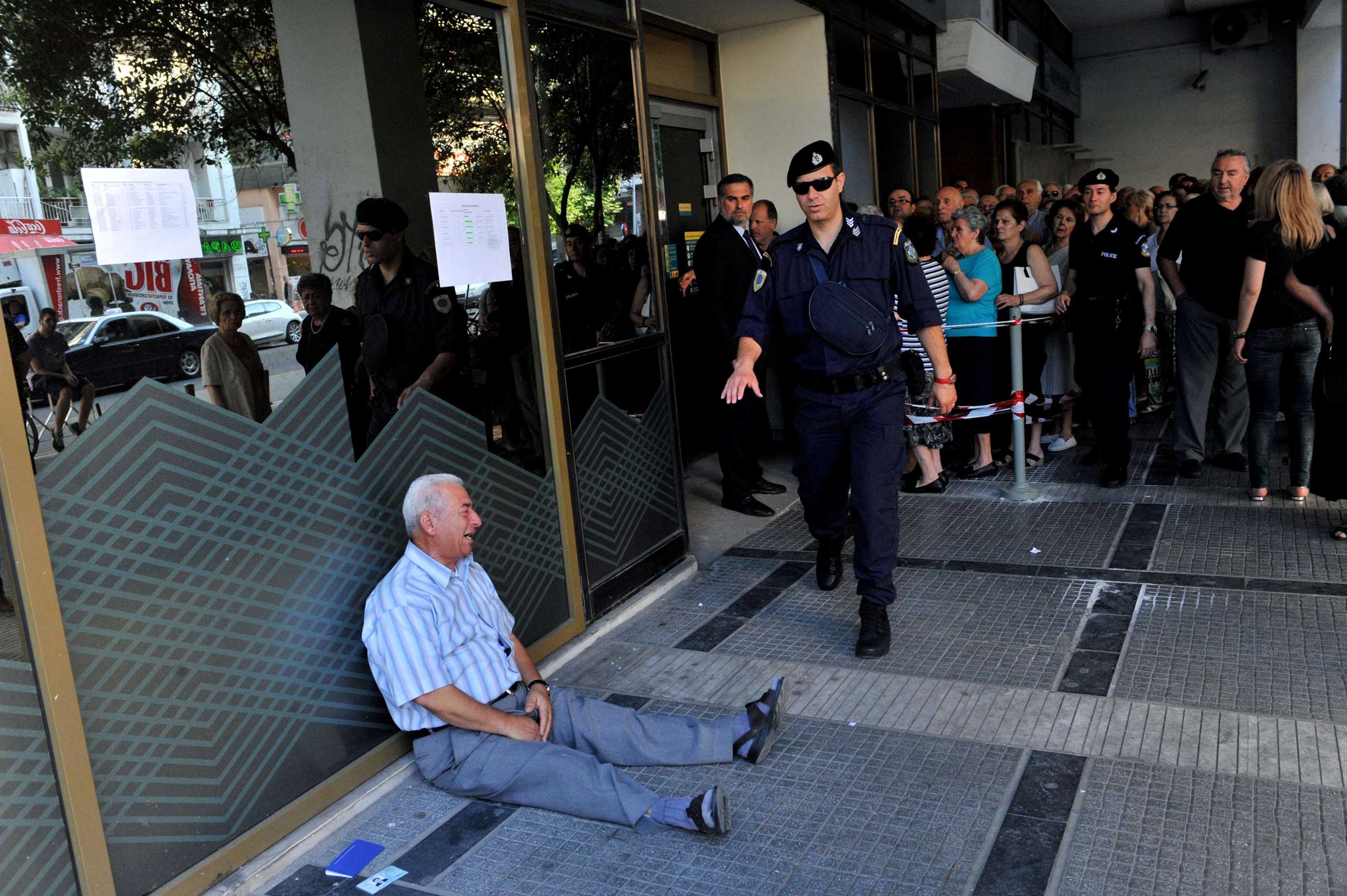 Giorgos Chatzifotiadis, sitting on the ground crying outside a national bank branch, as pensioners queue to withdraw their pensions, with a limit of 120 euros, in Thessaloniki, on July 3, 2015. (Sakis Mitrolidis—AFP/Getty Images)