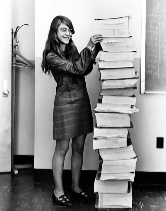 Margaret Hamilton standing next to listings of the actual Apollo Guidance Computer (AGC) source code.