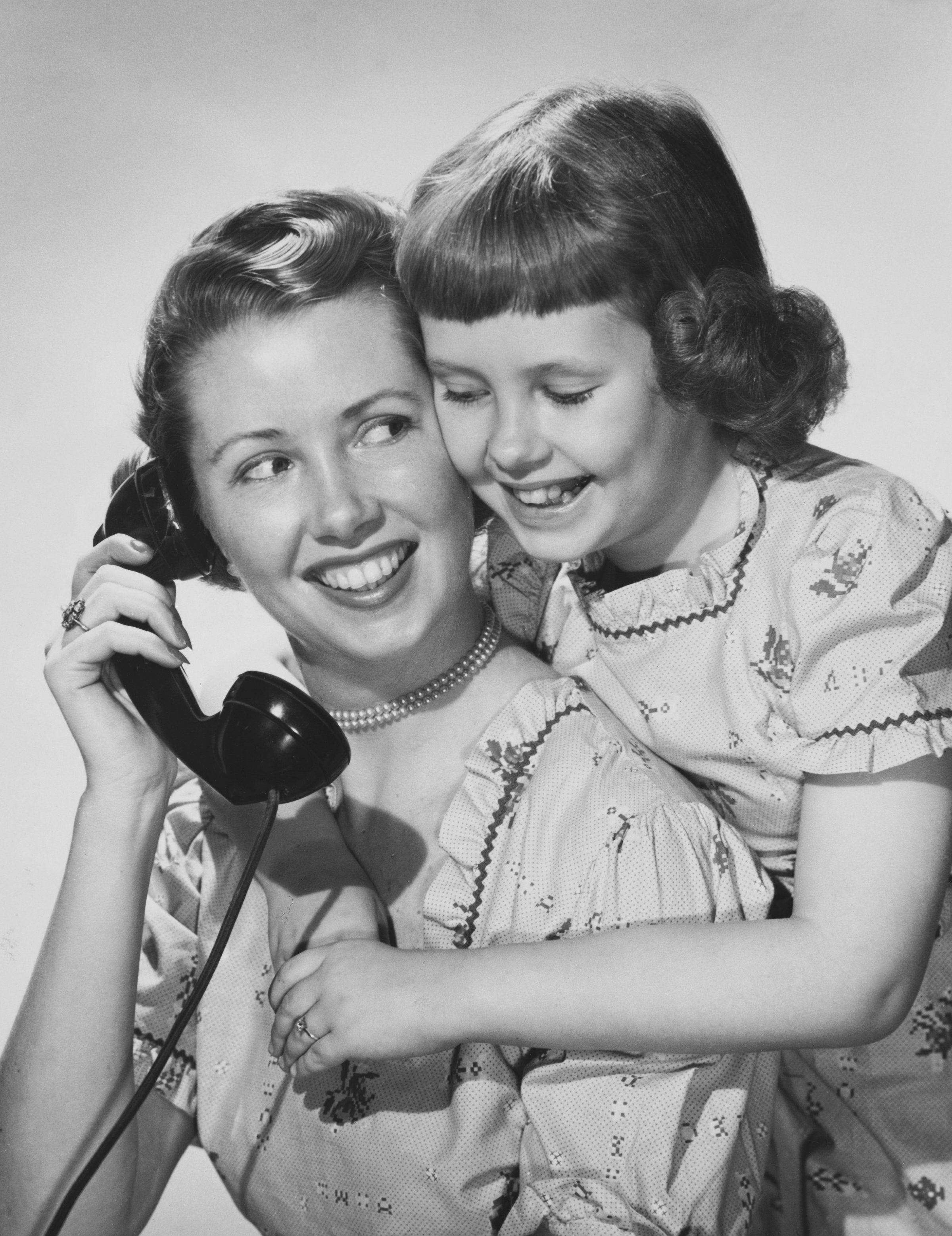 Mother holding telephone and hugging daughter (12-13)