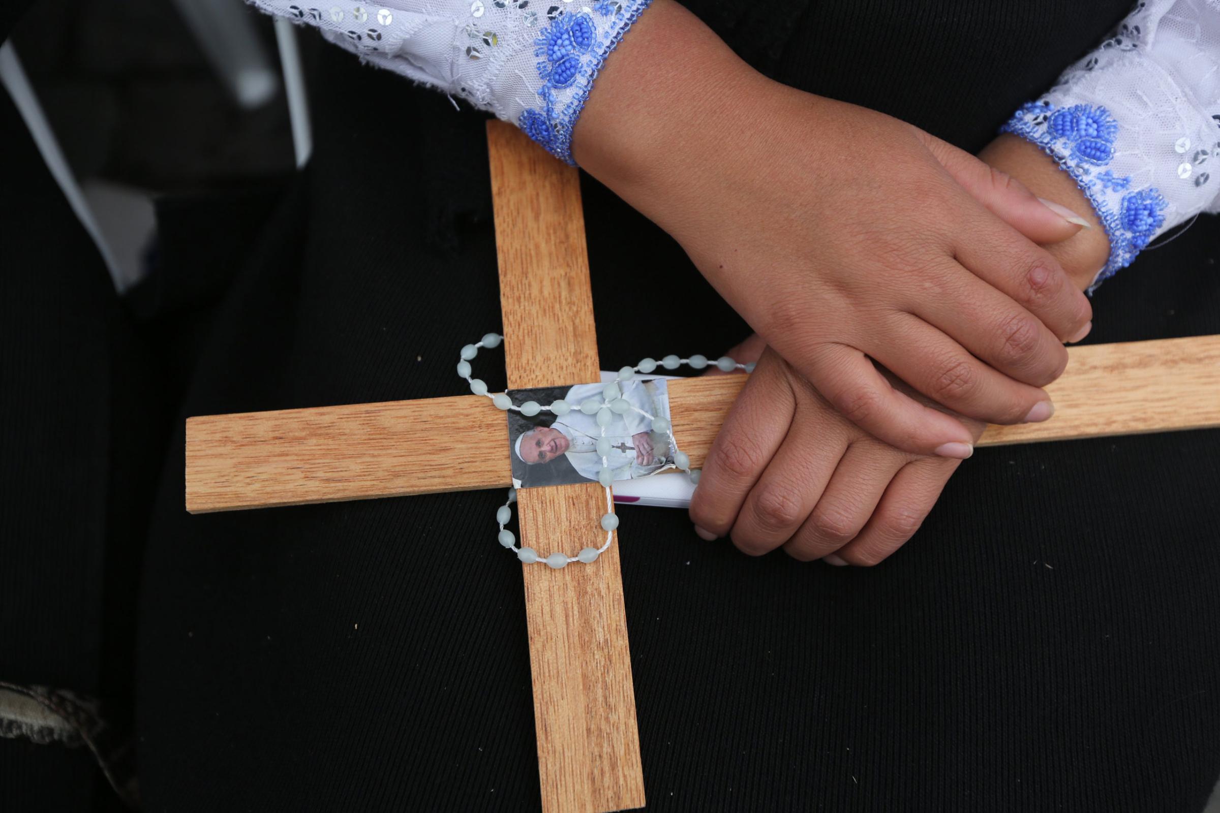 A woman holds a rosary and a wooden cross with an image of Pope Francis as she waits for the arrival of the Pontiff in San Francisco square, Quito, Ecuador, Tuesday, July 7, 2015. Francis is scheduled to meet with members of Ecuador's civil society and give and address in San Francisco Church. (AP Photo/Fernando Llano)