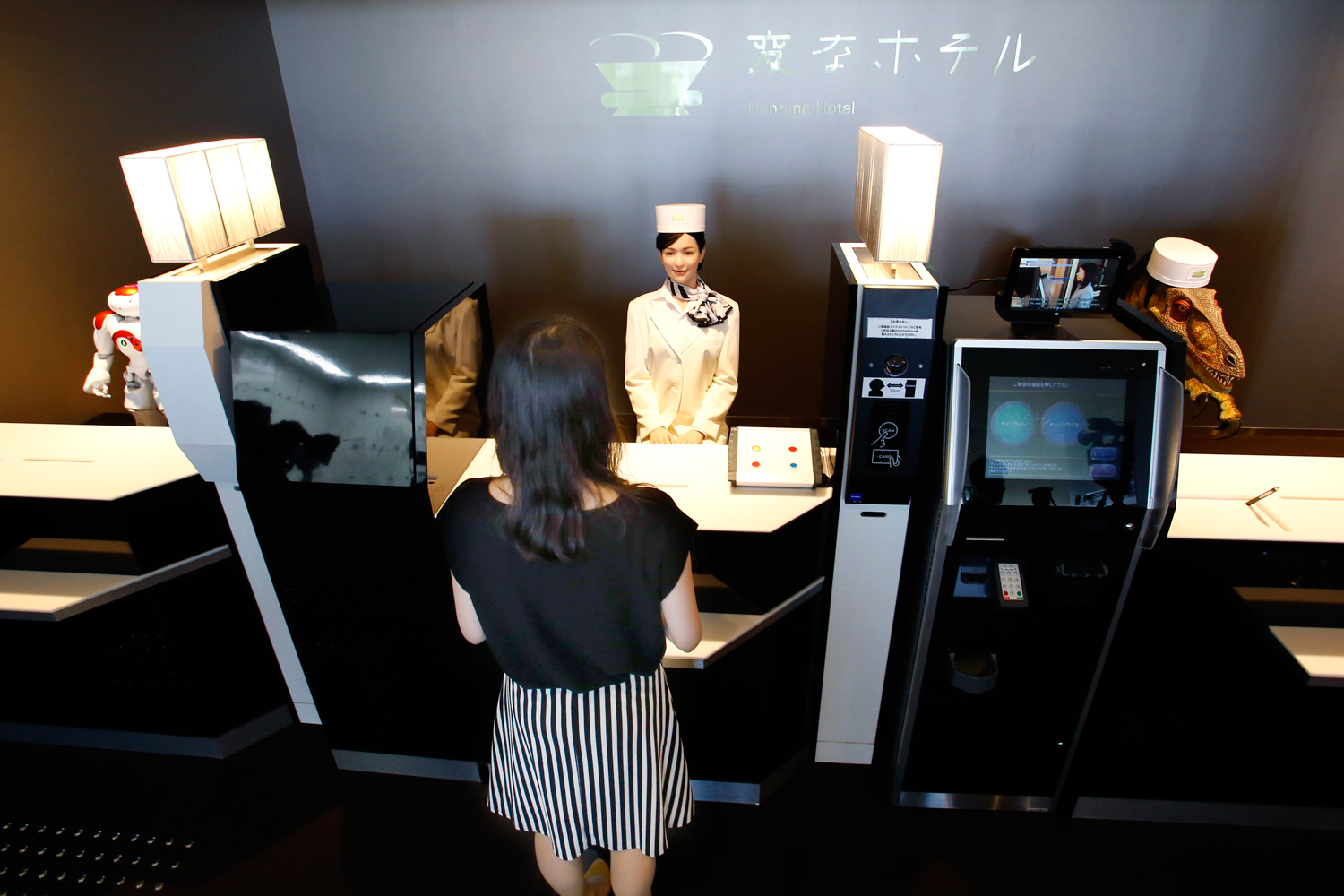 A receptionist robot, top center, accompanied by two other robots, greets a hotel employee demonstrating how to check in the new hotel, aptly called Henn na Hotel or Weird Hotel, in Sasebo, southwestern Japan, July 15, 2015 (Shizuo Kambayashi—AP)