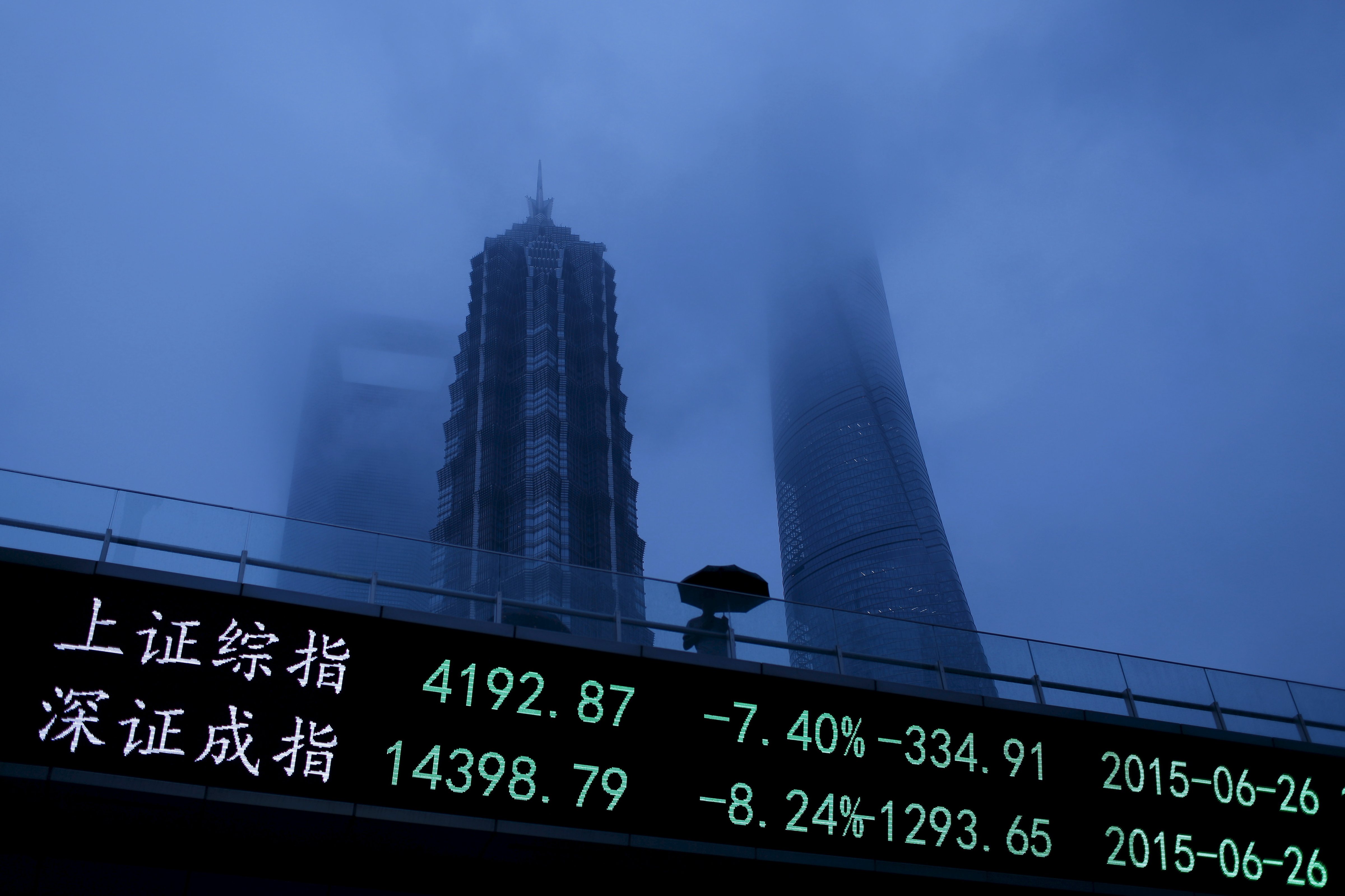 A man walks past an electronic board showing the benchmark Shanghai and Shenzhen stock indices, on a pedestrian overpass at the Pudong financial district in Shanghai, China, June 26, 2015. (Aly Song—Reuters)