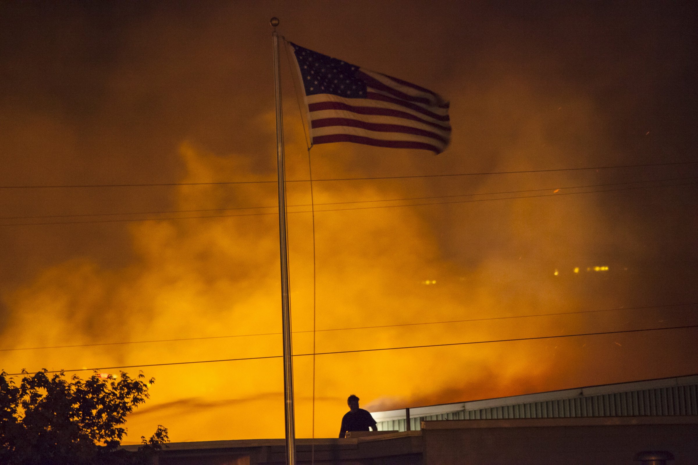 A U.S. flag is seen as a commercial building burns after being ignited by the Sleepy Hollow fire in Wenatchee, Washington