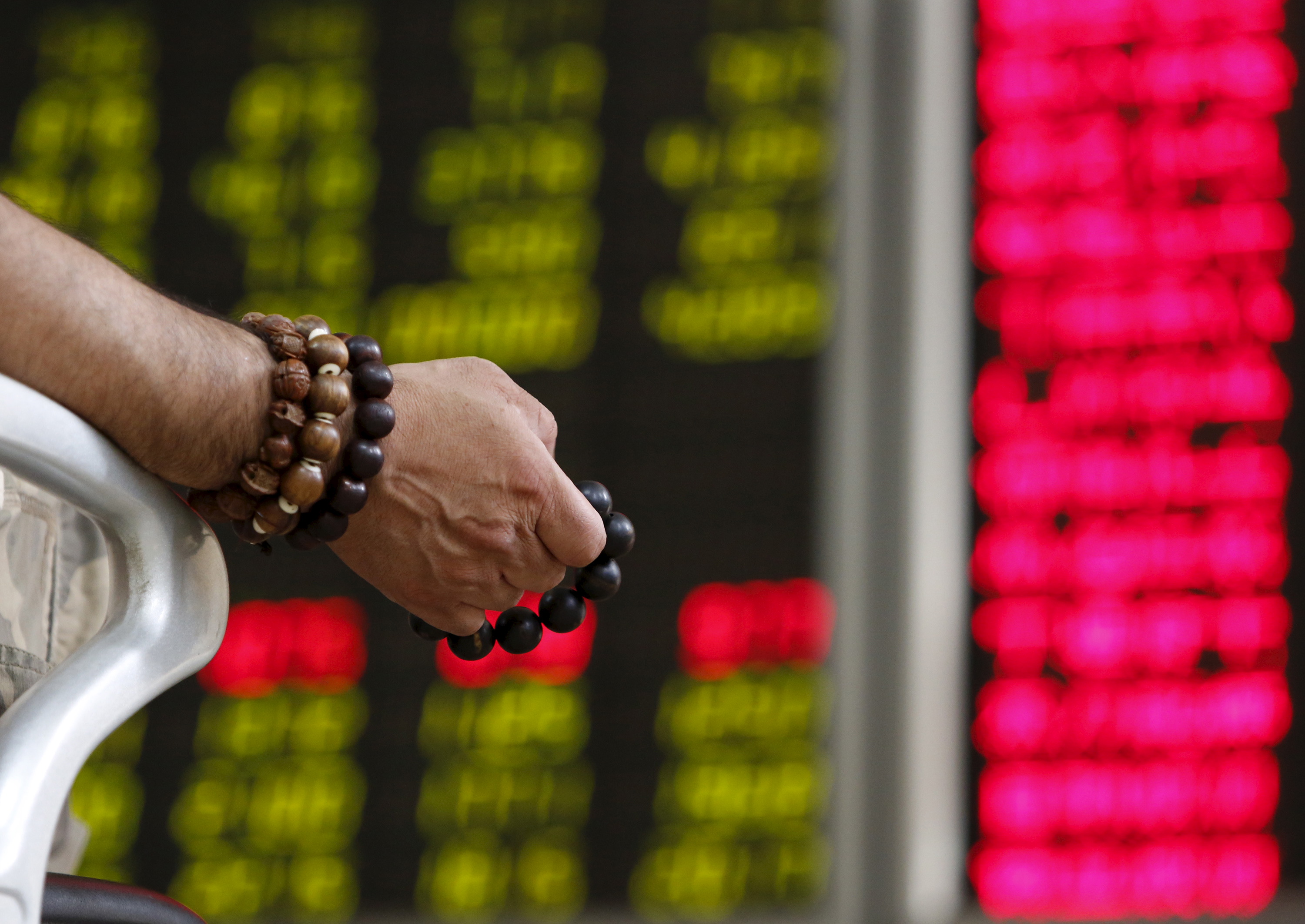 An investor holds onto prayer beads as he watches a board showing stock prices at a brokerage office in Beijing