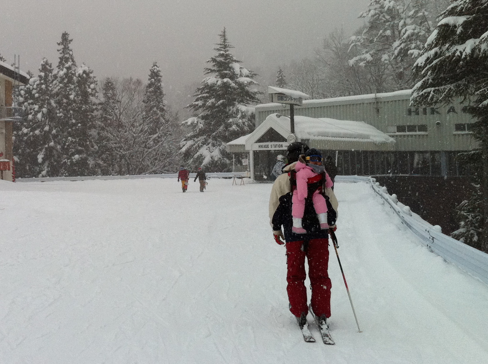 skier carrying kid in pink snowsuit