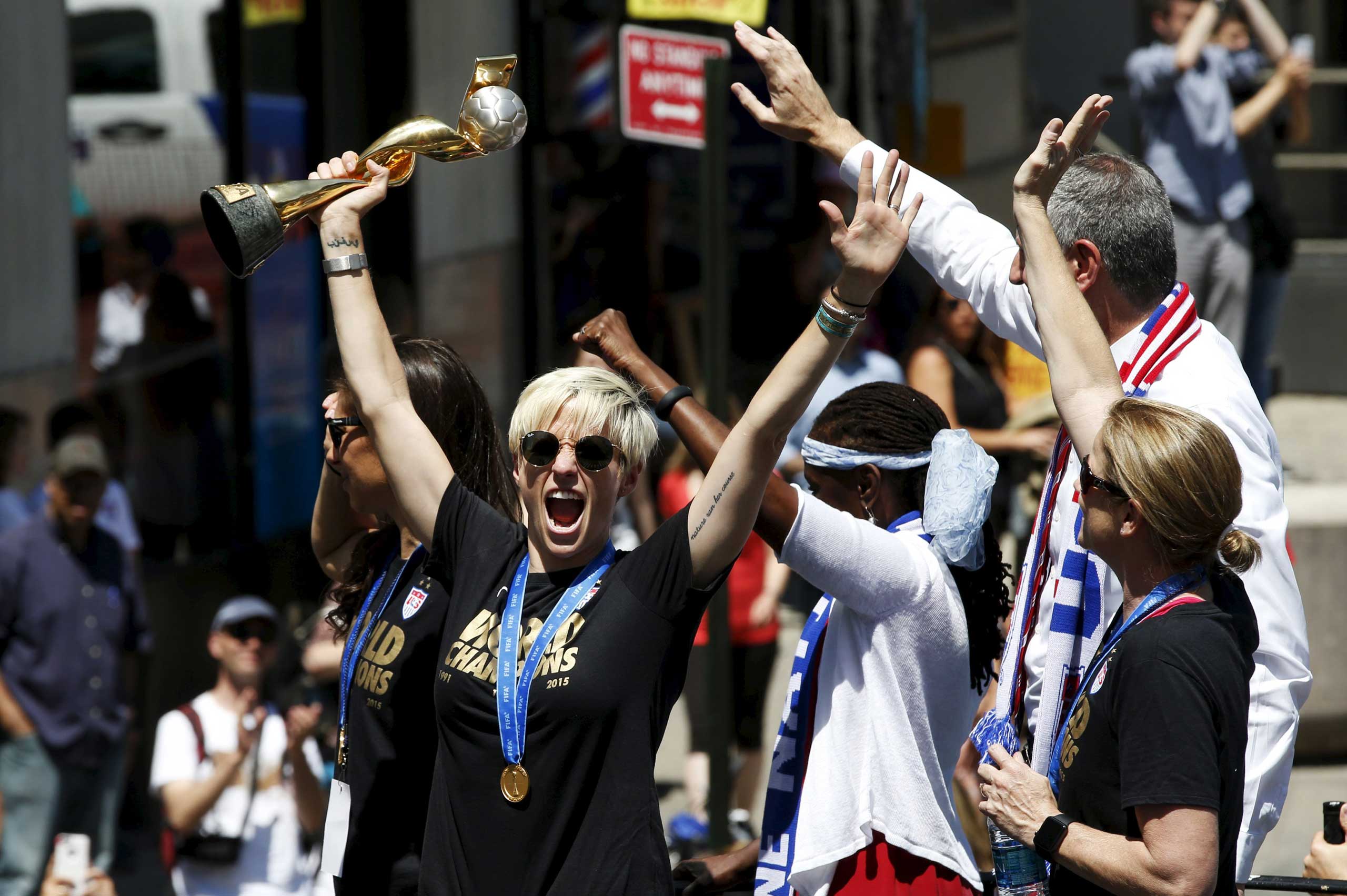 U.S. women's soccer player Megan Rapinoe holds the Wold Cup trophy as she rides a float with team mate Carli Lloyd and New York Mayor Bill de Blasio during the ticker tape parade in New York City on July 10, 2015.
