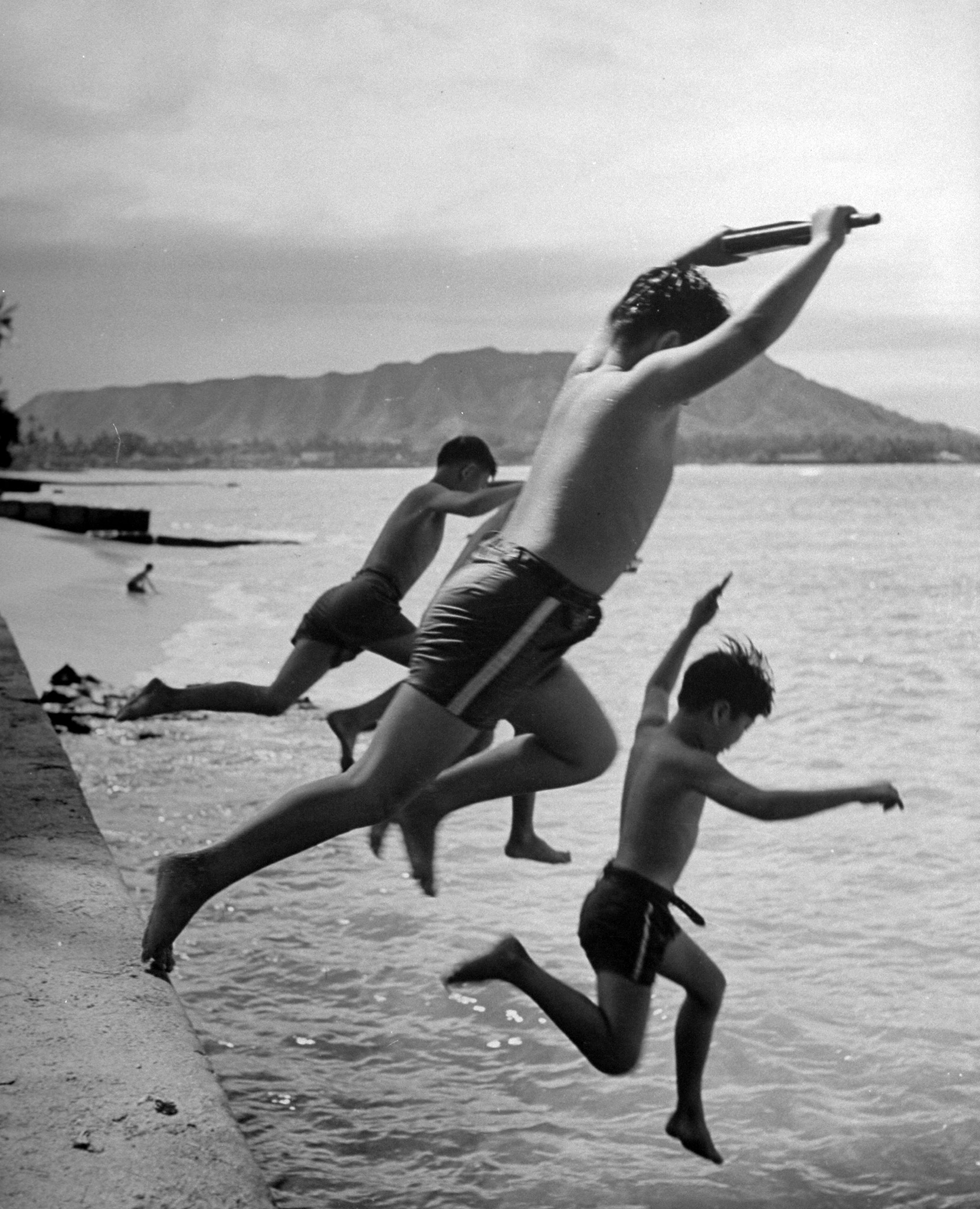 Japanese boys jumping from sea wall while playing as soldiers in American army.