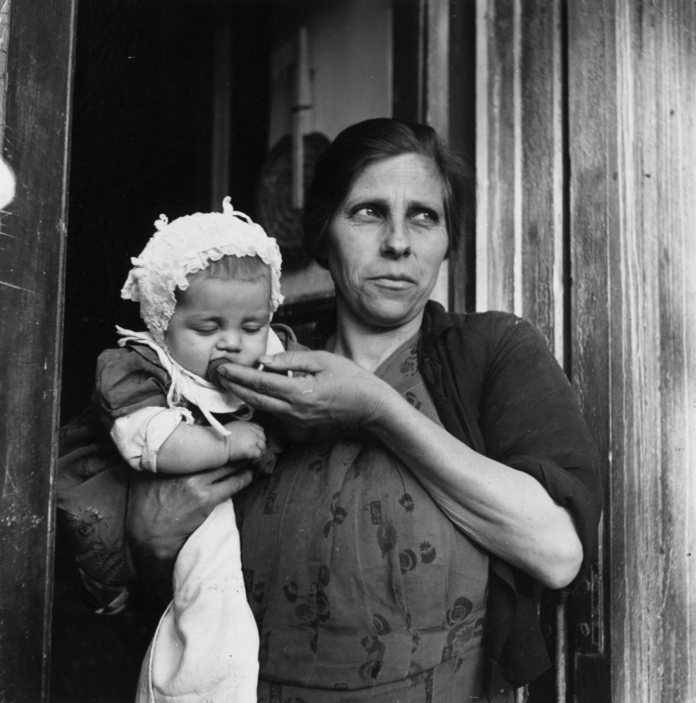 An Italian woman holding a baby in the doorway of her home in Naples, 1950.