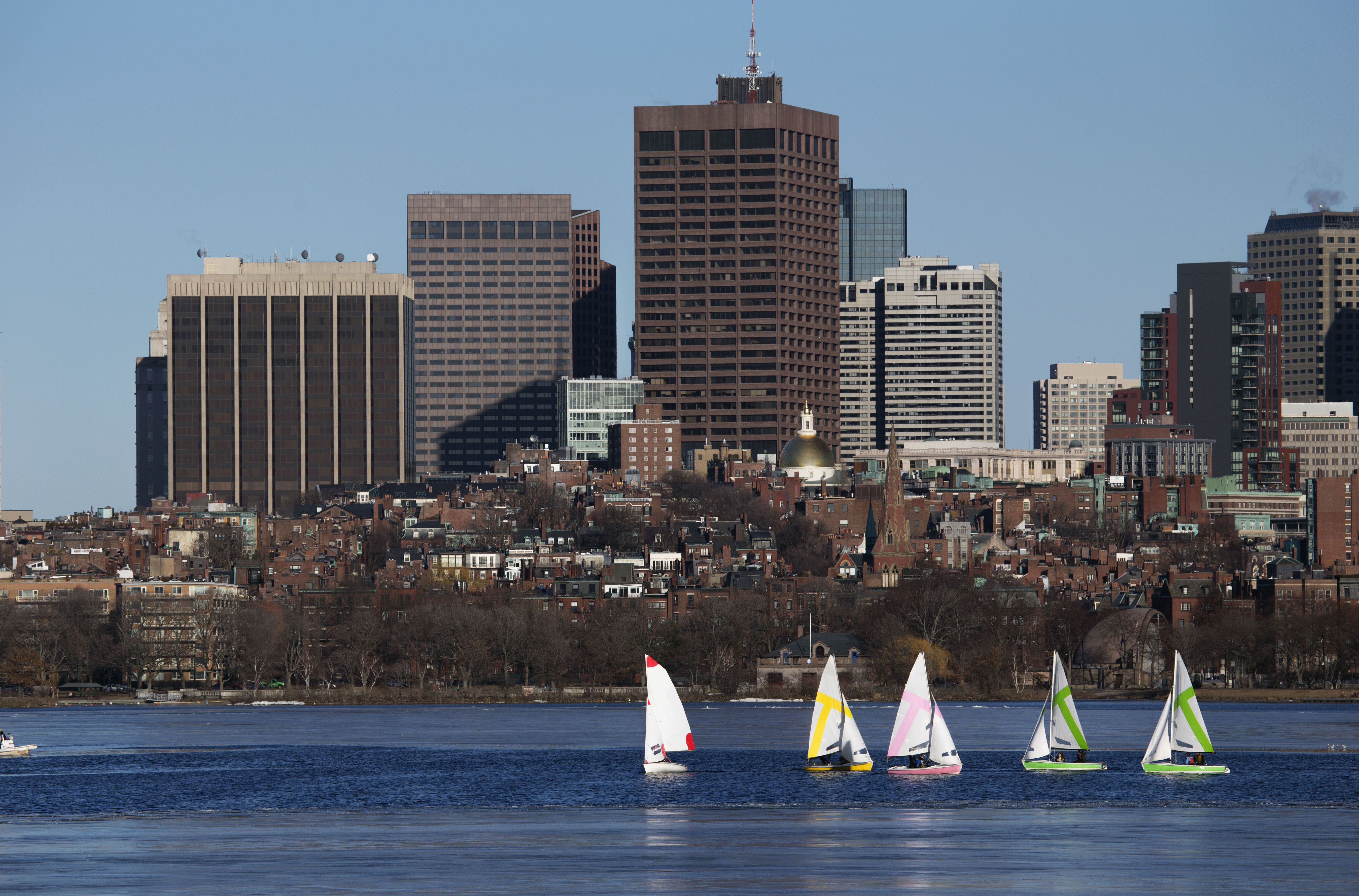 Colorful docked sailboats and Boston Skyline in winter on half frozen Charles River, Massachusetts