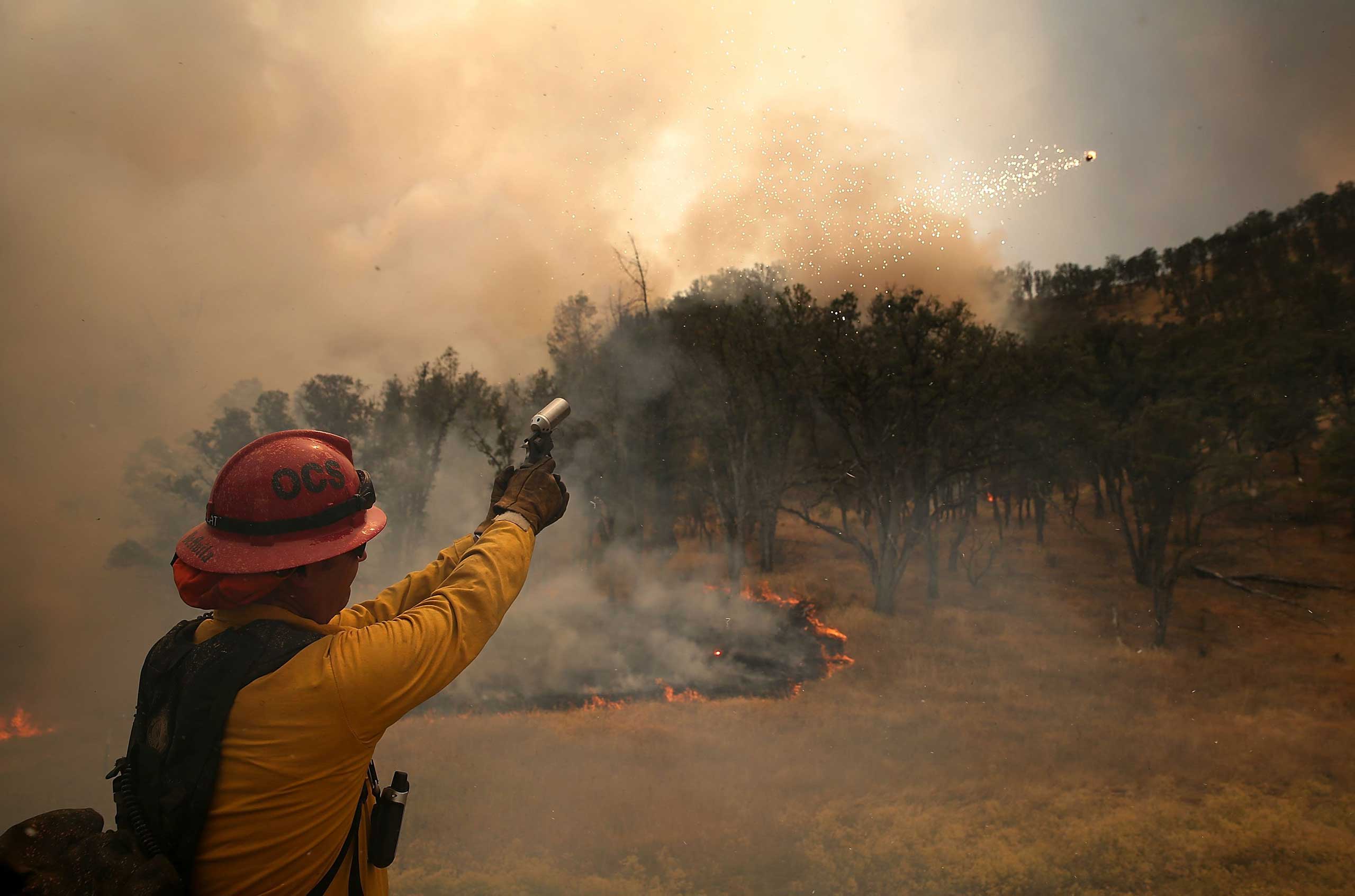 Oceanside Fire Department captain Greg DeAvila shoots a flare into dry brush during a burn operation to head off the Rocky Fire near Clearlake, Calif. on Aug. 2, 2015.