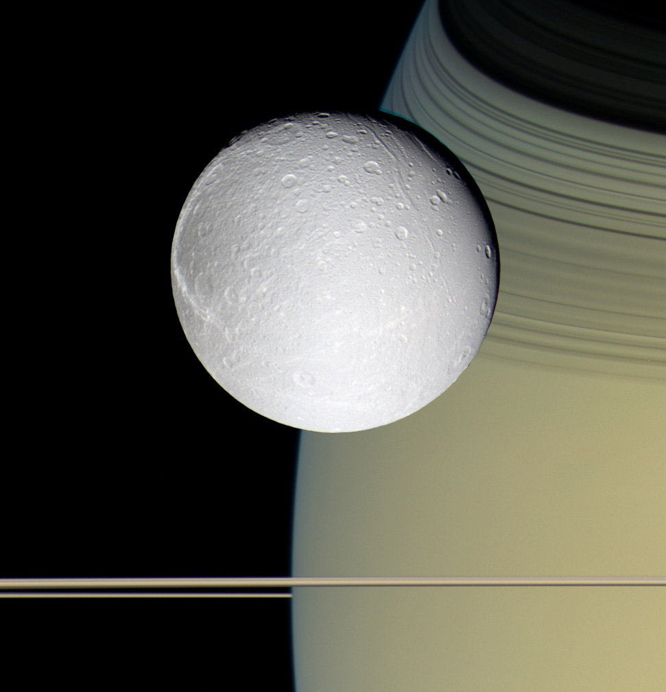 Speeding toward pale, icy Dione, Cassini's view is enriched by the tranquil gold and blue hues of Saturn in the distance. The horizontal stripes near the bottom of the image are Saturn's rings. The spacecraft was nearly in the plane of the rings when the images were taken, thinning them by perspective and masking their awesome scale. The thin, curving shadows of the C ring and part of the B ring adorn the northern latitudes visible here, a reminder of the rings' grandeur.It is notable that Dione, like most of the other icy Saturnian satellites, looks no different in natural color than in monochrome images.Images taken on Oct. 11, 2005, with blue, green and infrared (centered at 752 nanometers) spectral filters were used to create this color view, which approximates the scene as it would appear to the human eye. The images were obtained with the Cassini spacecraft wide-angle camera at a distance of approximately 39,000 kilometers (24,200 miles) from Dione and at a Sun-Dione-spacecraft, or phase, angle of 22 degrees. The image scale is about 2 kilometers (1 mile) per pixel.