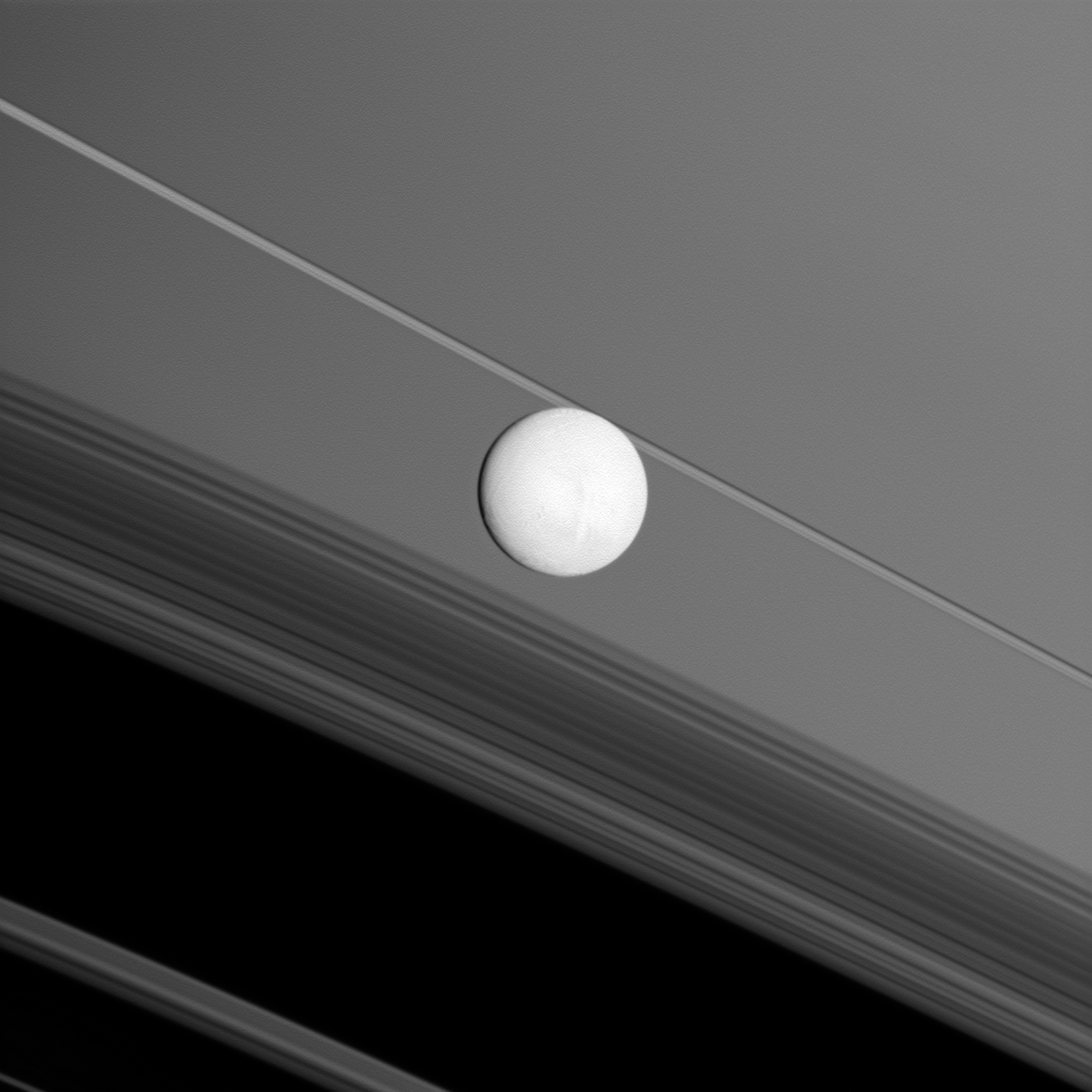 Saturn's moon Enceladus brightly reflects sunlight before a backdrop of the planet's rings.